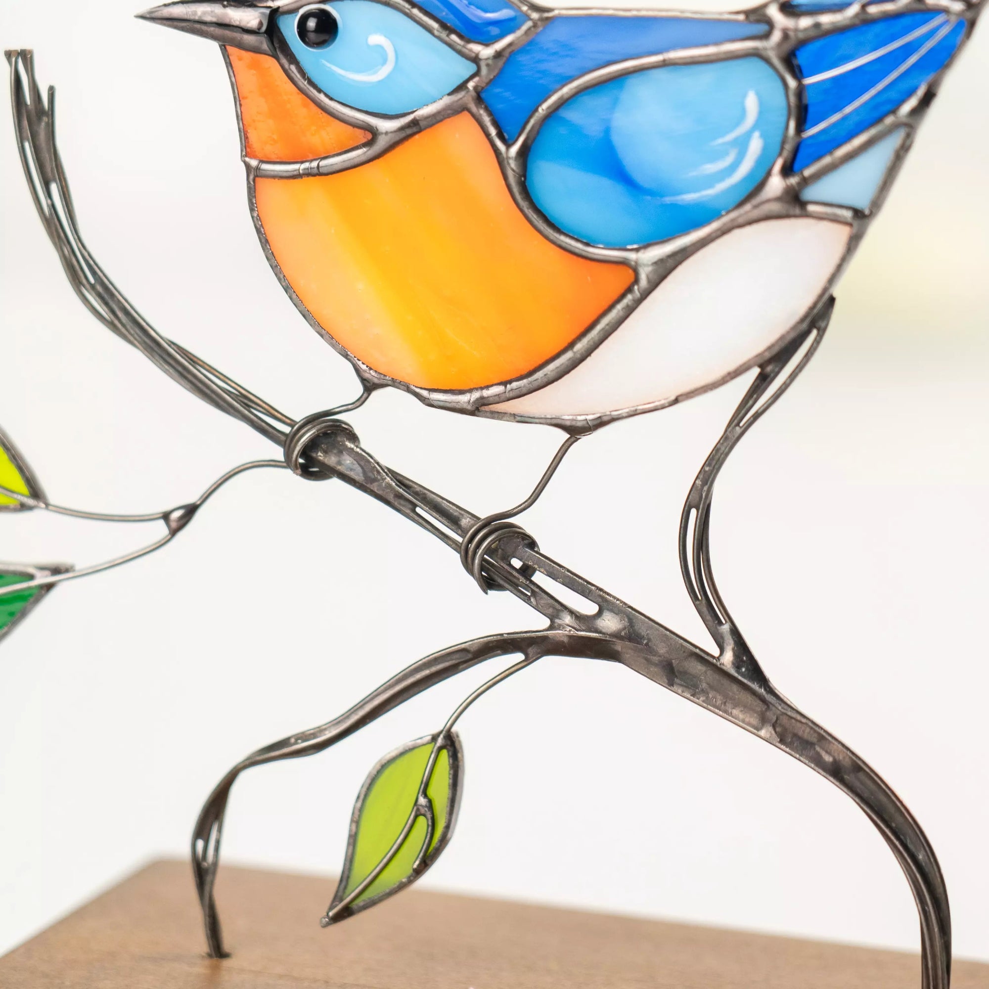 Zoomed-in image of bluebird with stained glass wings, orange chest, and green leaves in the background