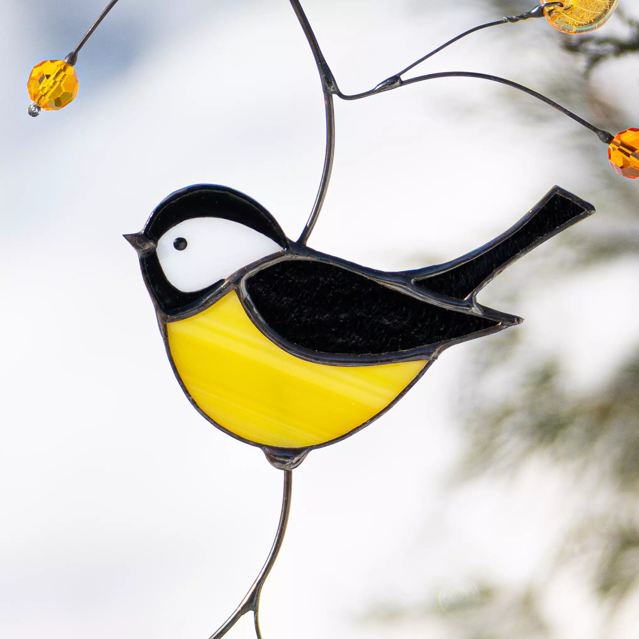 Zoomed view of a yellow and black stained glass chickadee with amber bead accents