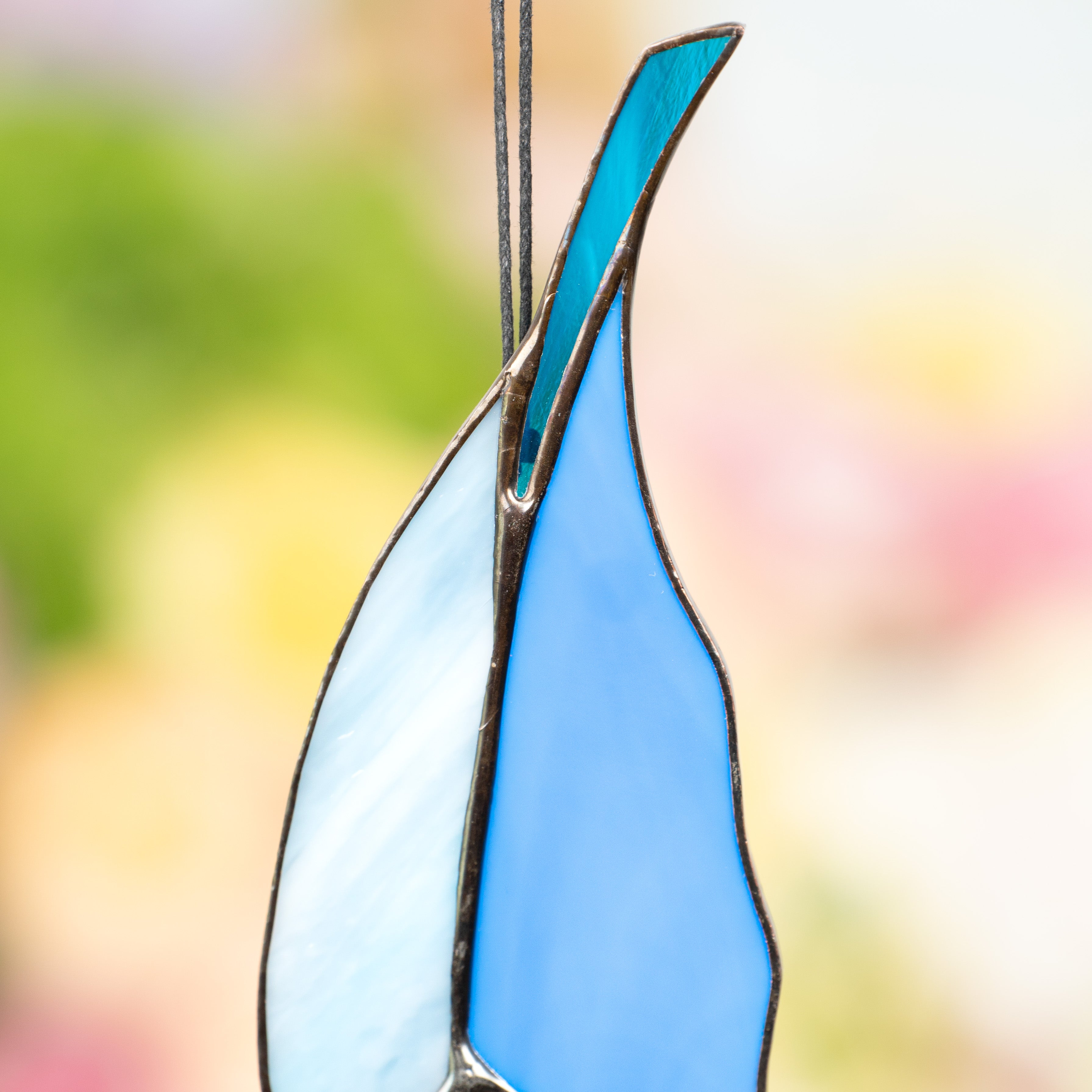 Macro view of stained glass feather’s blue and light blue top with a sturdy loop for secure hanging.