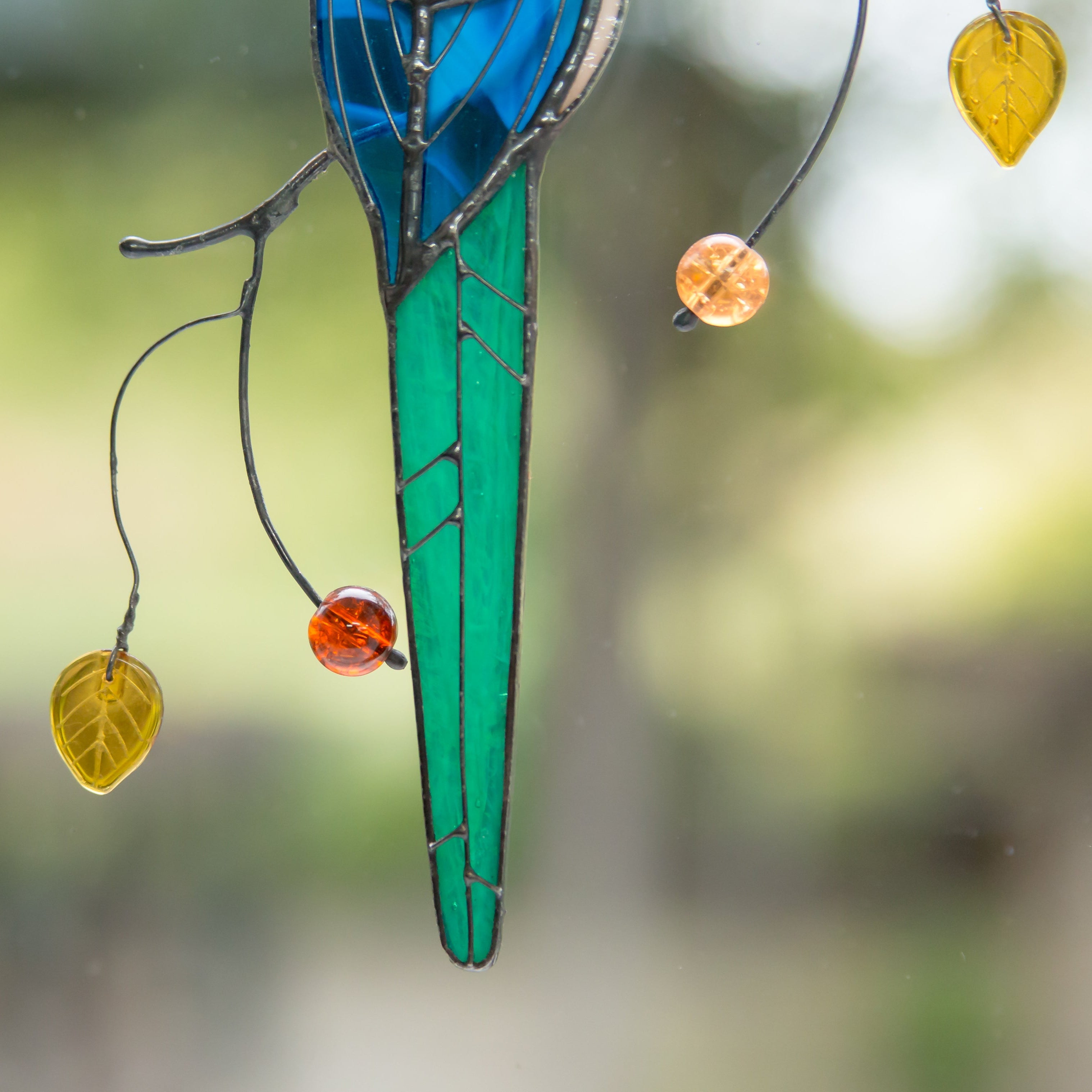 Focus on the green tail of the stained glass magpie, featuring delicate leaf and bead details.