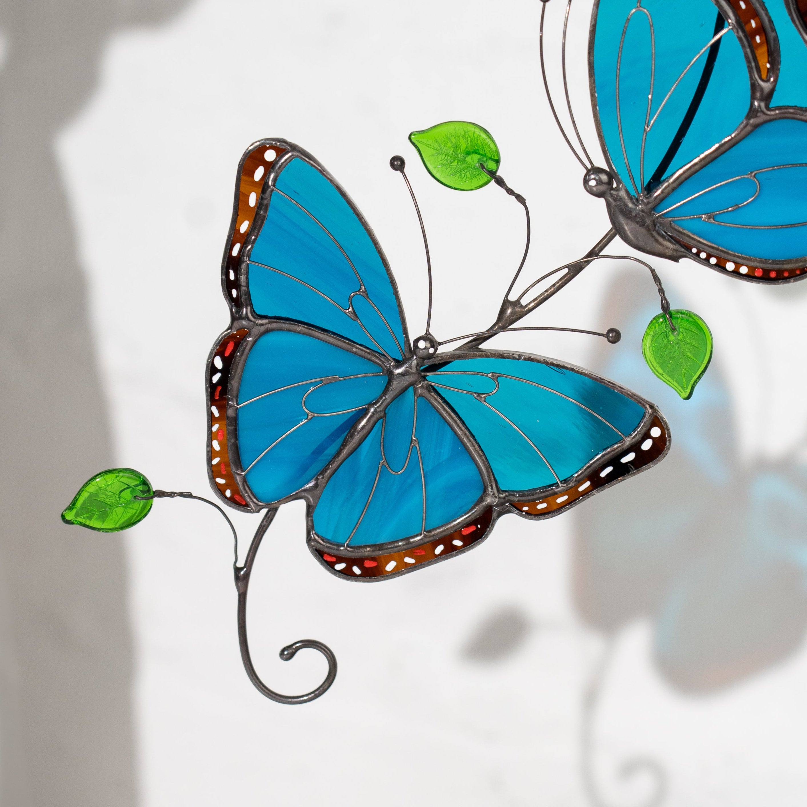 Detailed view of stained glass morpho butterflies with vibrant blue wings and green decorative glass leaves.