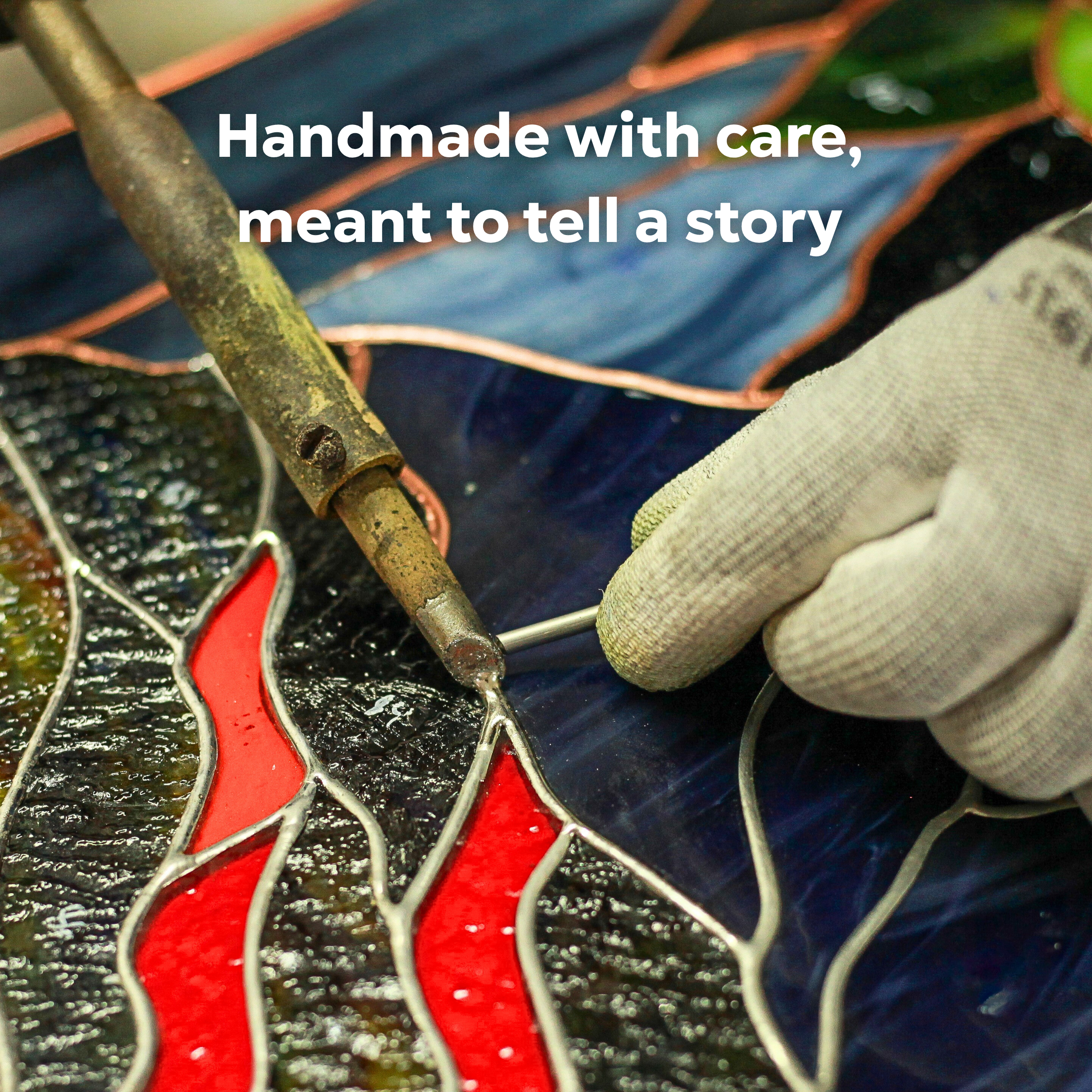 Hand soldering red stained glass pieces during the creation process of a panel, showing craftsmanship.