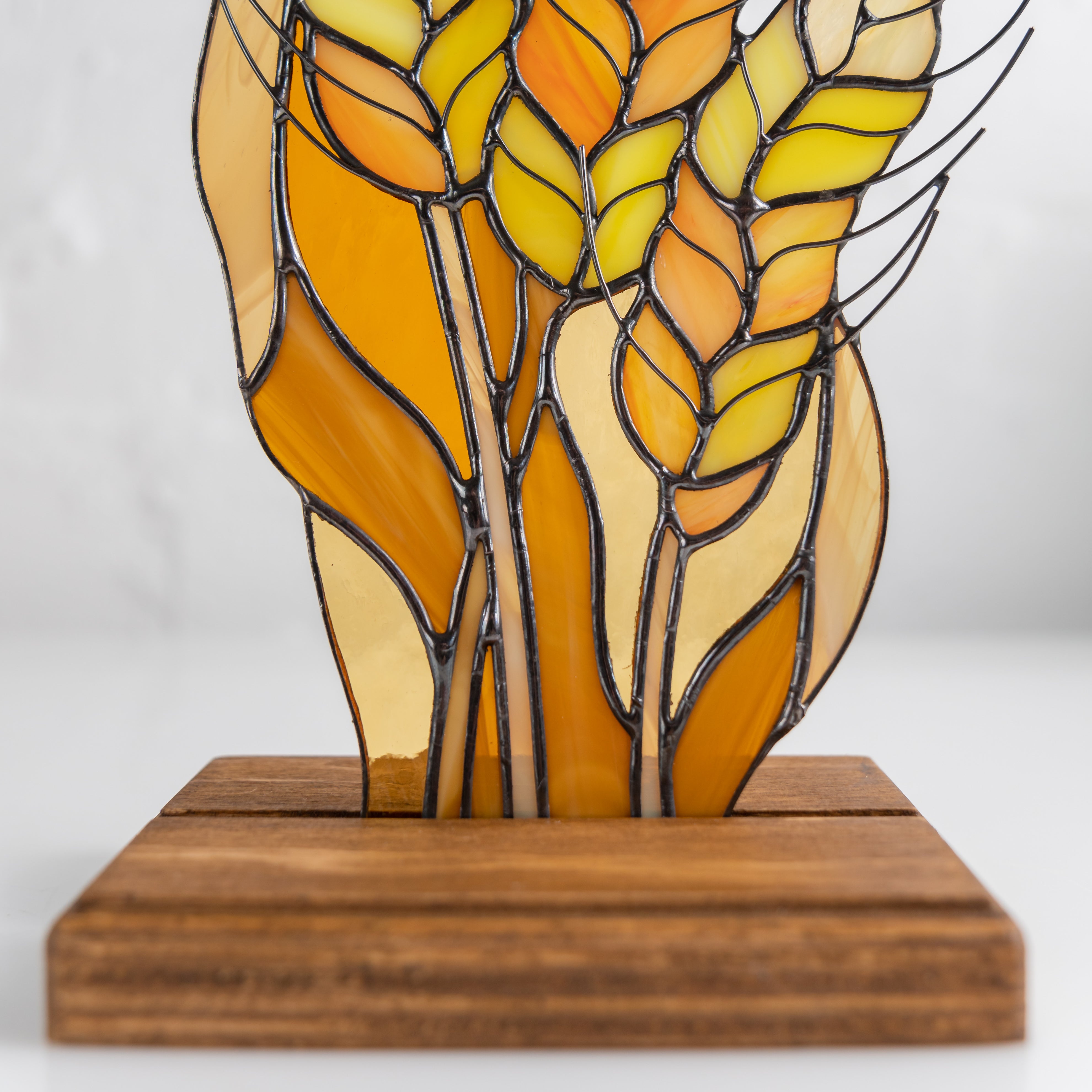 Detail view of stained glass wheat showing individual yellow and orange grain segments in metal outlines.