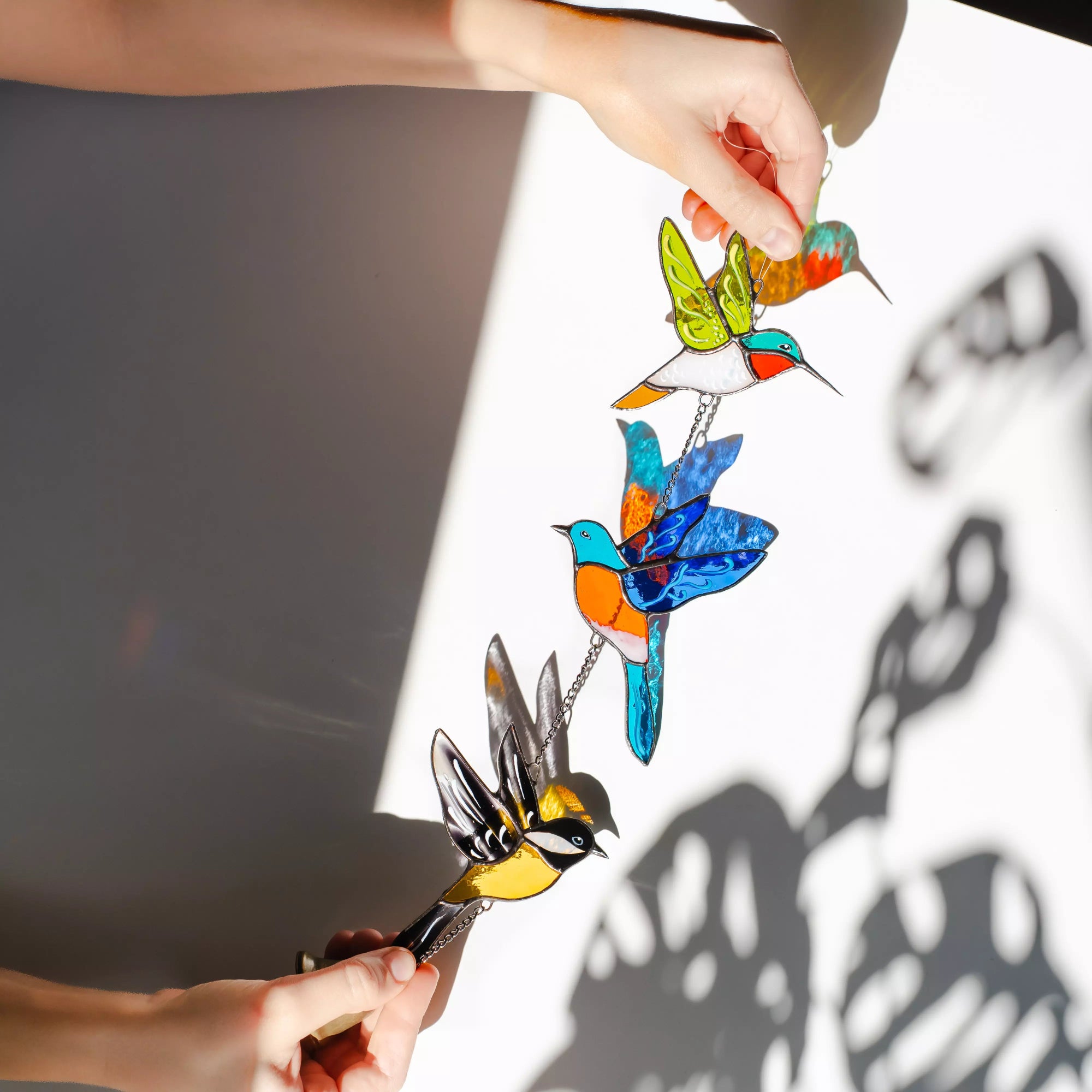Stained glass bird-shaped wind chime held by a person with a neutral background