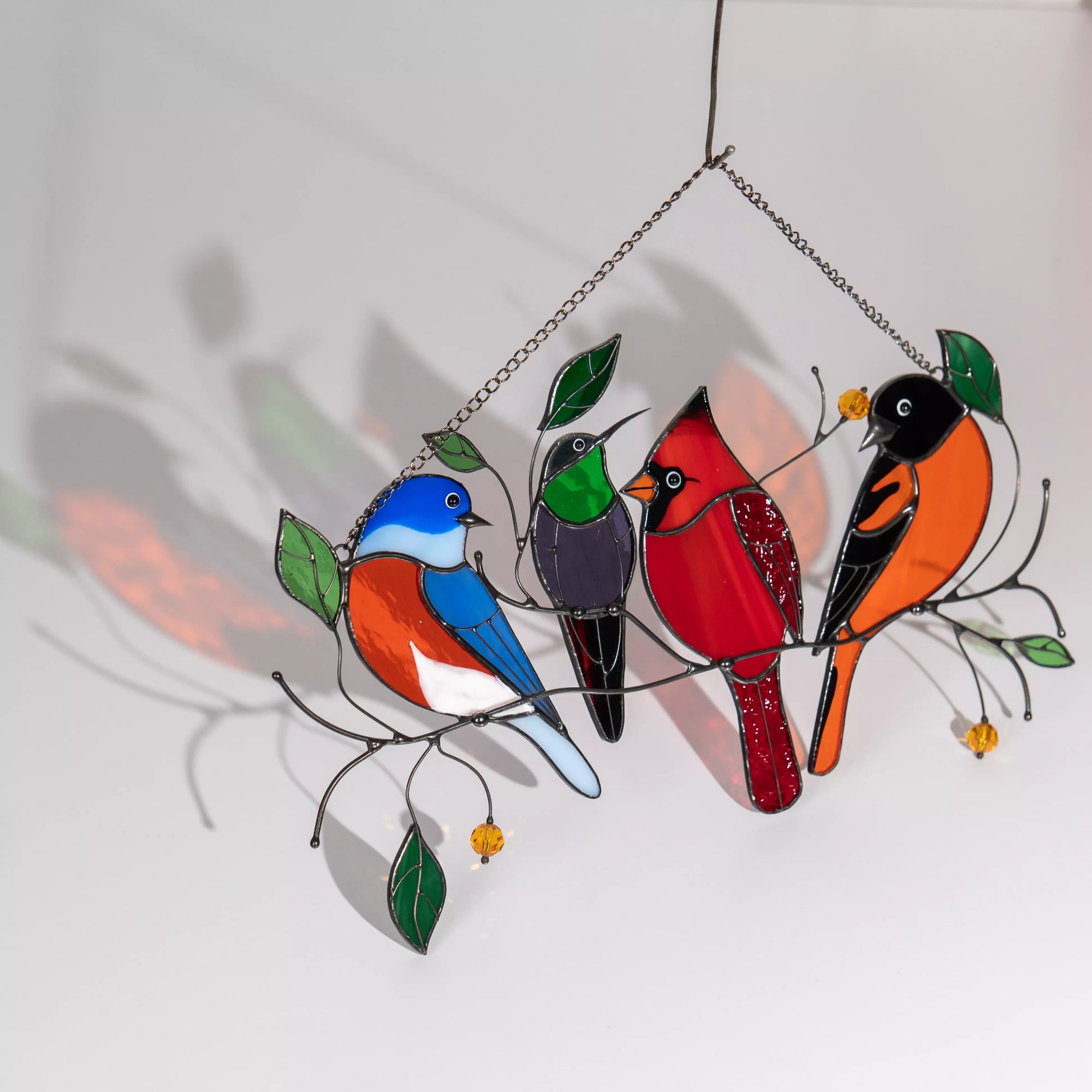 Colorful stained glass four birds on a branch with leaves, casting a colorful shadow on a white background
