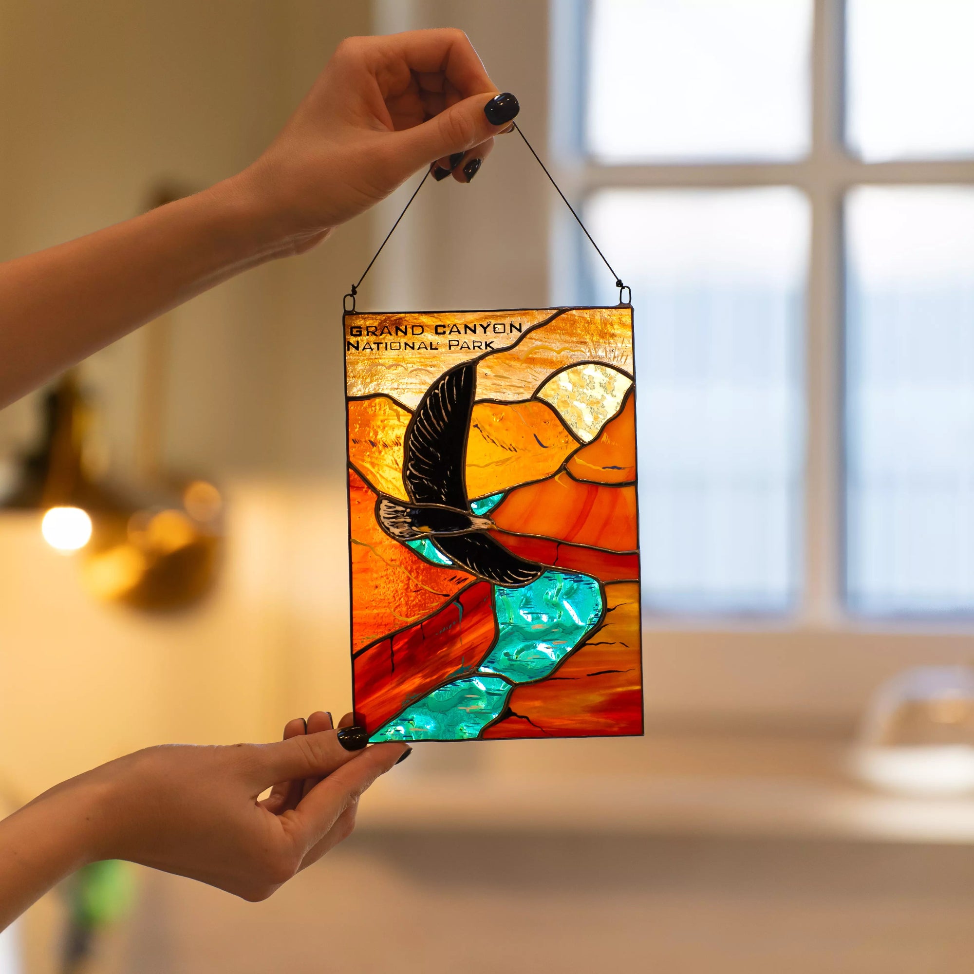 A person holding the Grand Canyon National Park stained glass panel in a warm, cozy interior setting.