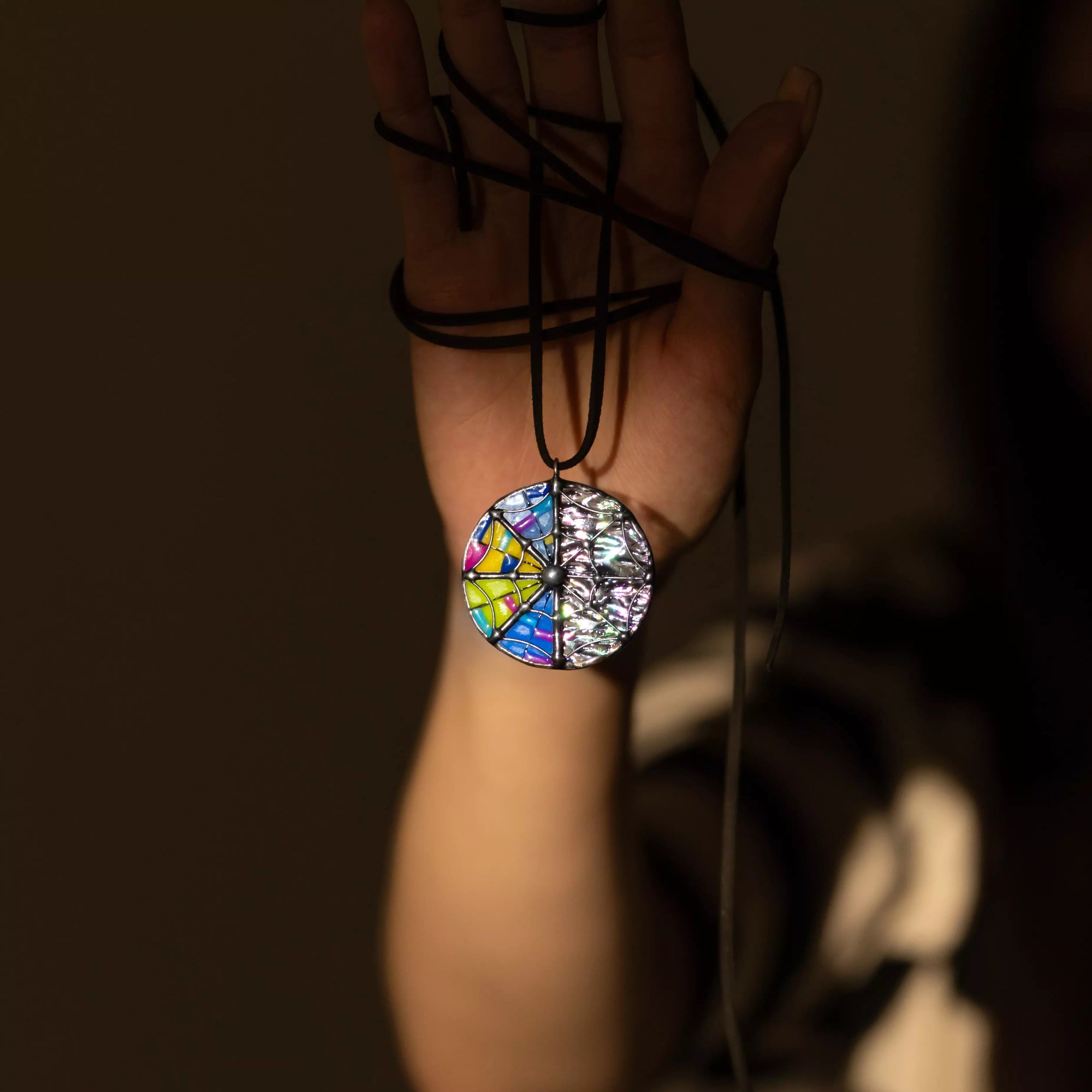 Necklace with a colorful stained glass pendant with web held by a hand against a dark background