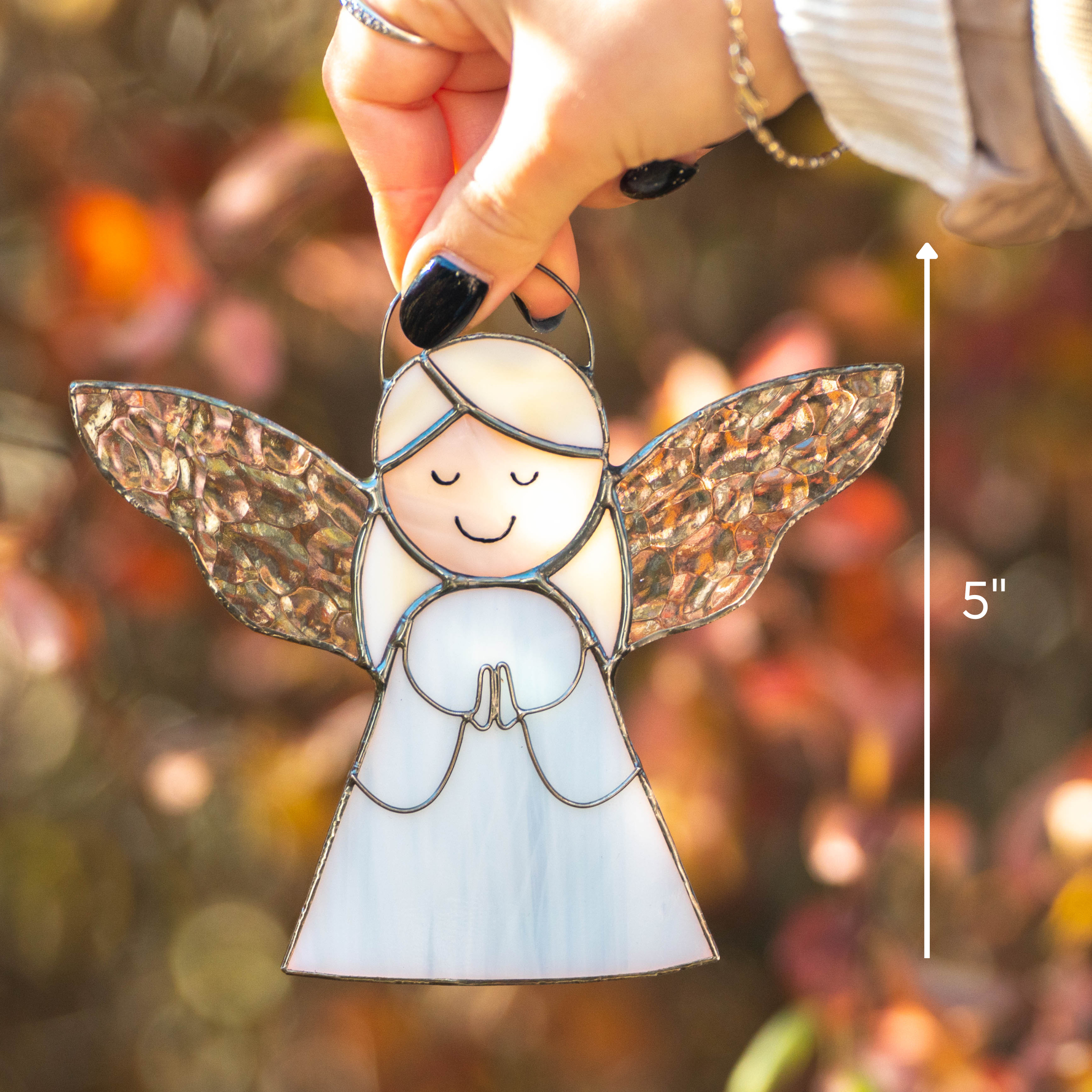 Close-up of a hand holding a stained glass angel suncatcher with clear textured wings and size marked as 5".