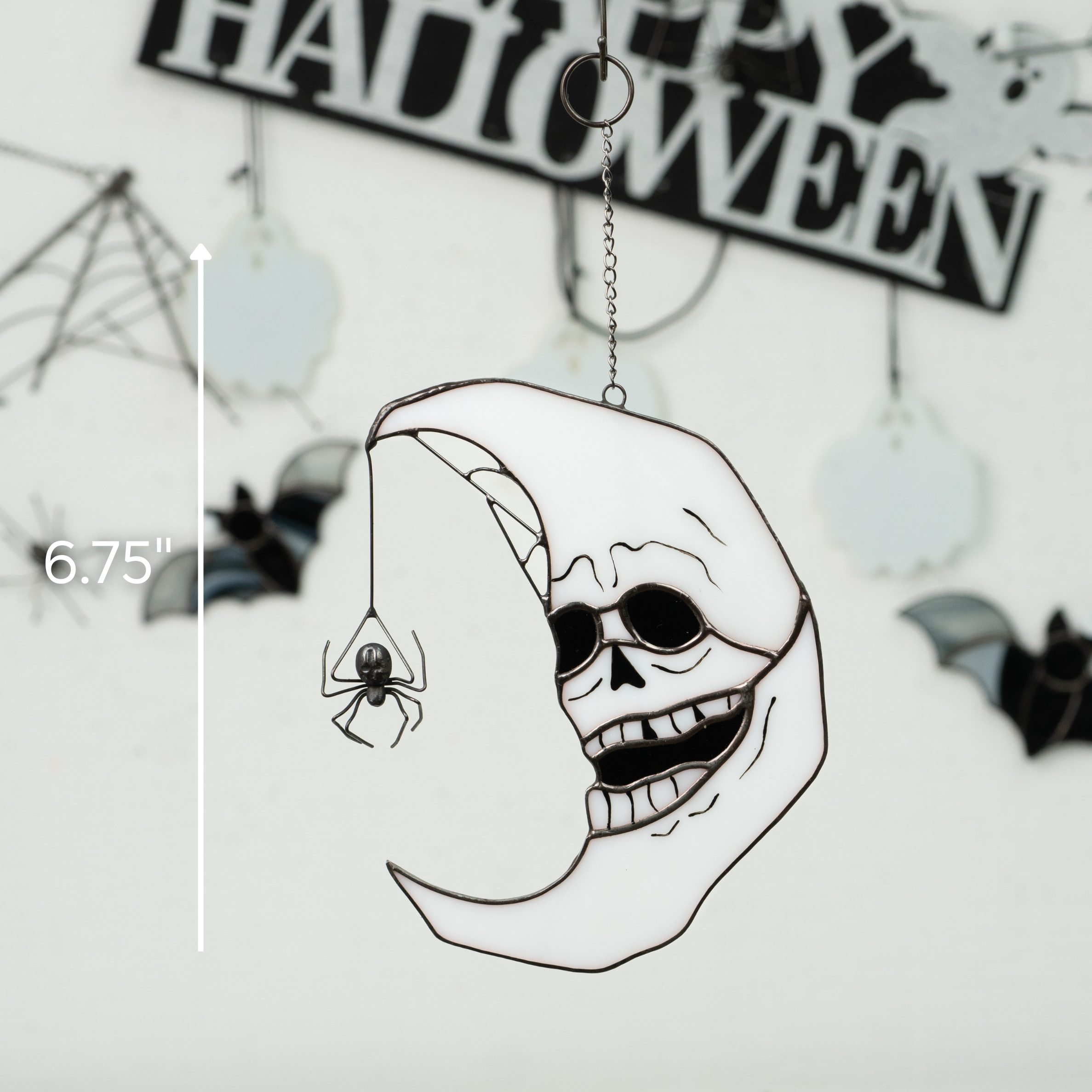 Skull moon glass suncatcher hanging on a branch with Halloween decor in the background and a size label 6.75"