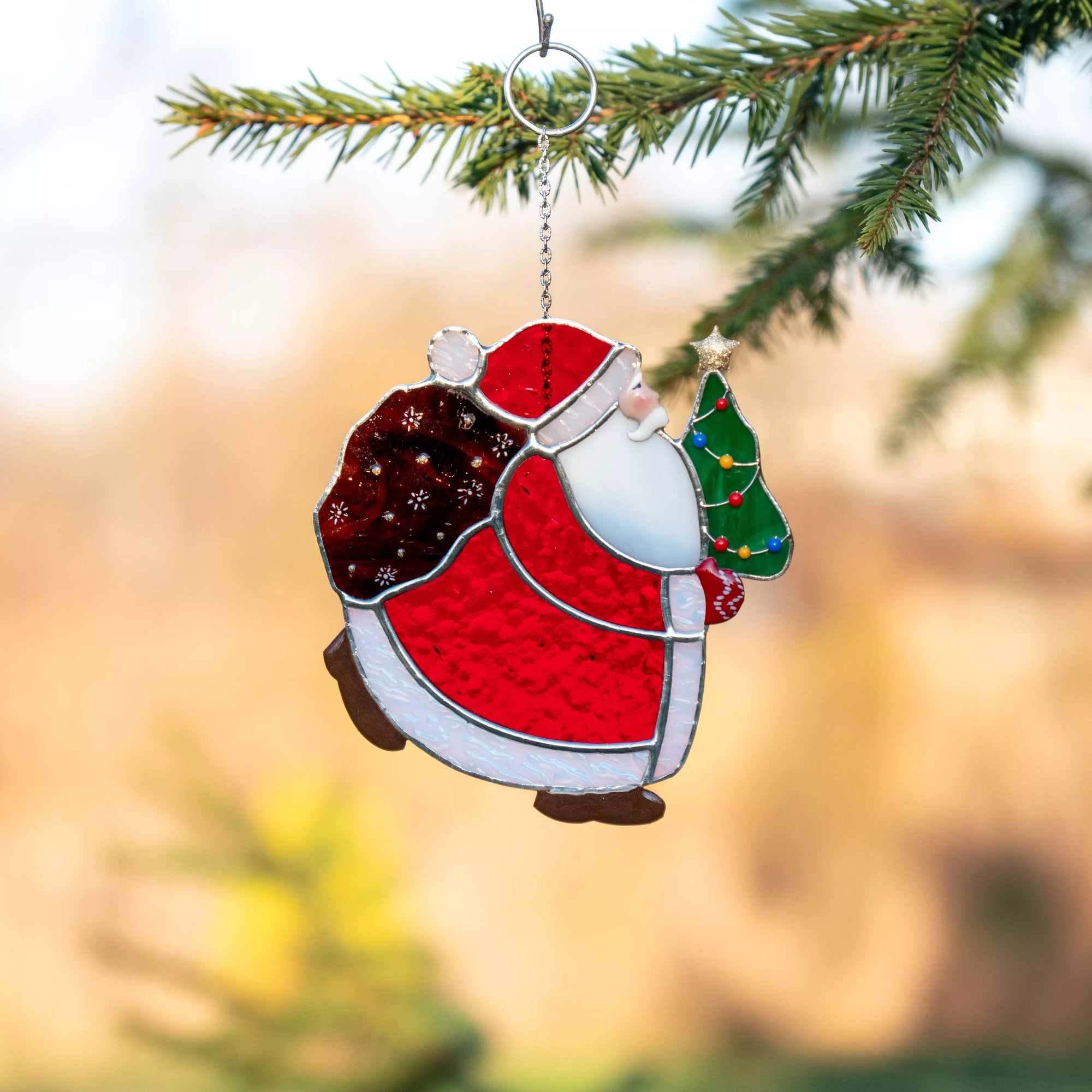 Stained glass Christmas suncatcher of a Santa Claus figure with a tree on a blurred green background