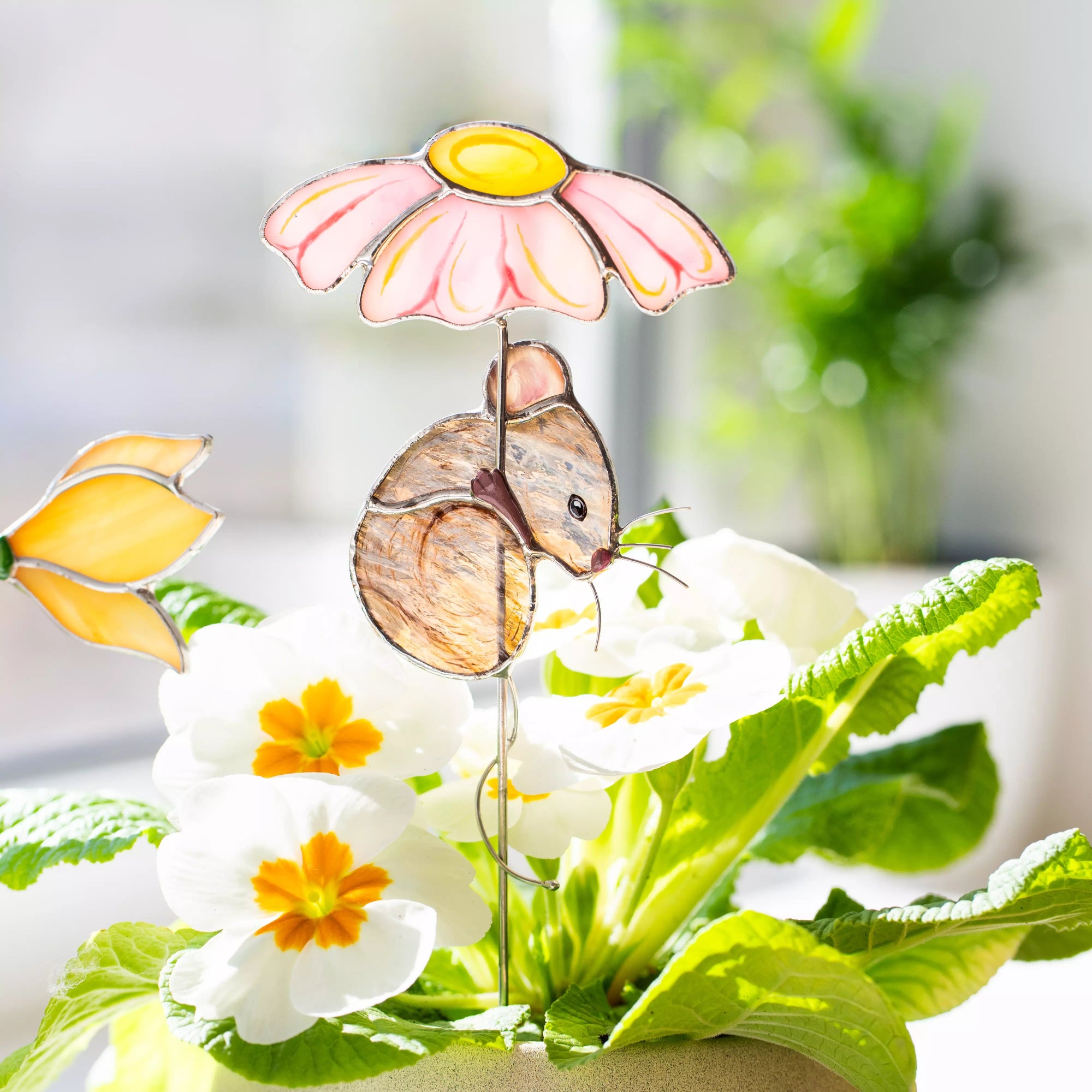 Stained glass plant stake with a mouse holding a pink flower umbrella among flowers and leaves.