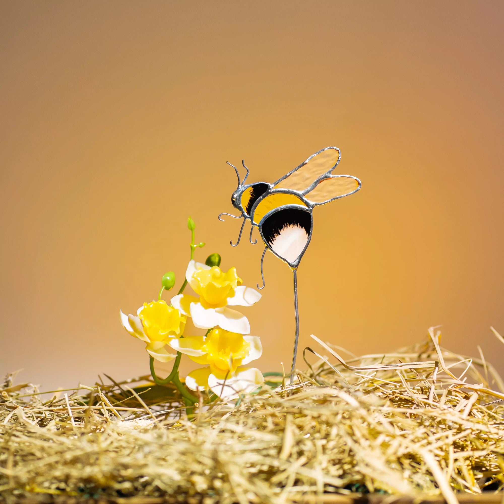 Stained glass bee plant stake on a yellow flower with a warm background