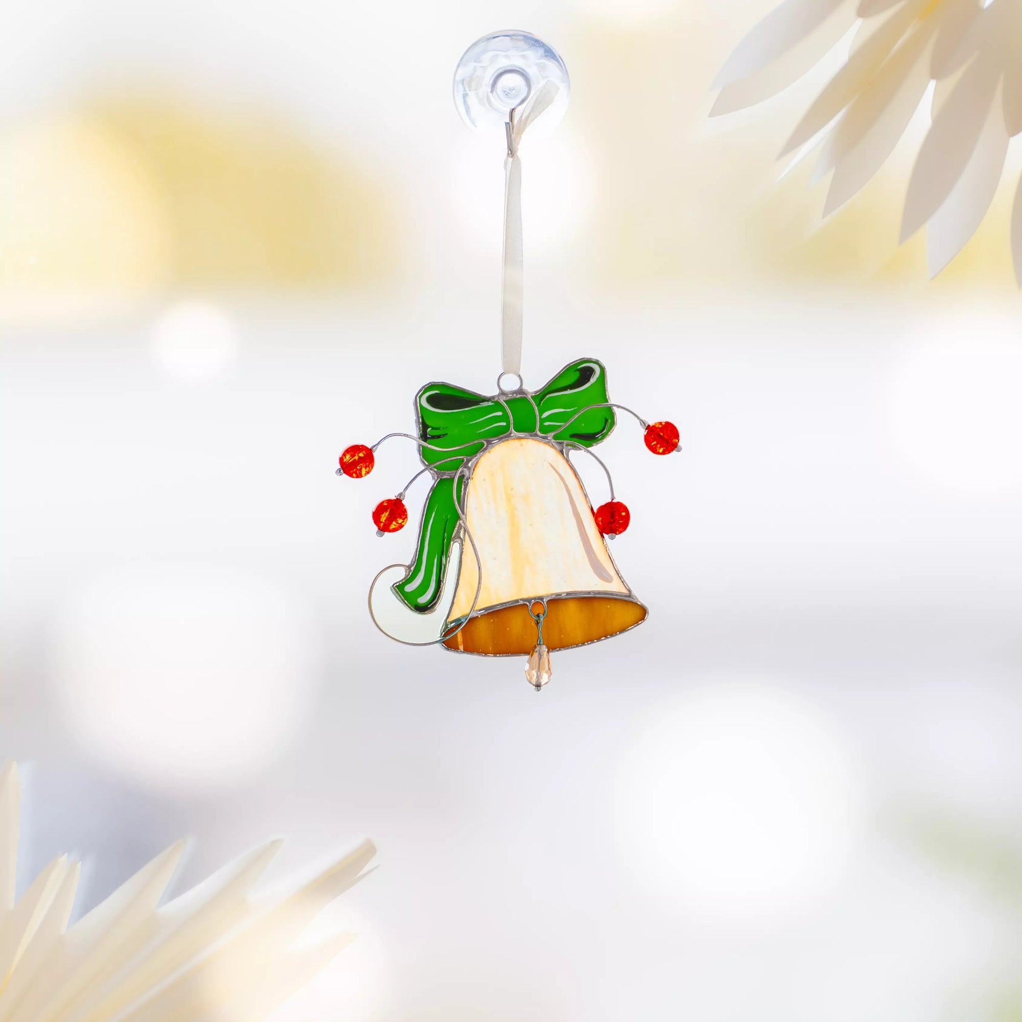 Stained glass bell with green bow and red beads hanging on a window
