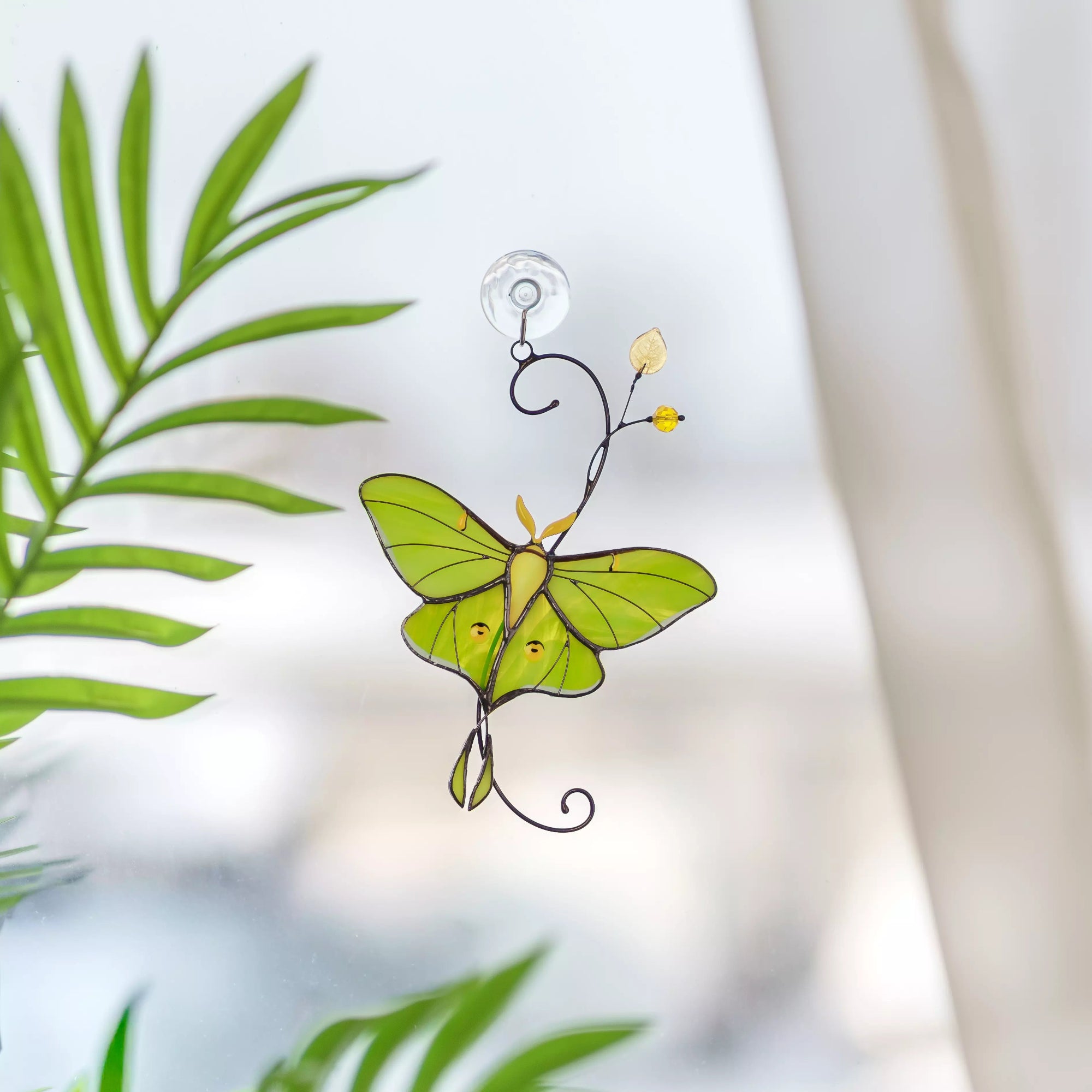 Stained glass luna moth butterfly hanging ornament with green wings on a blurred natural background