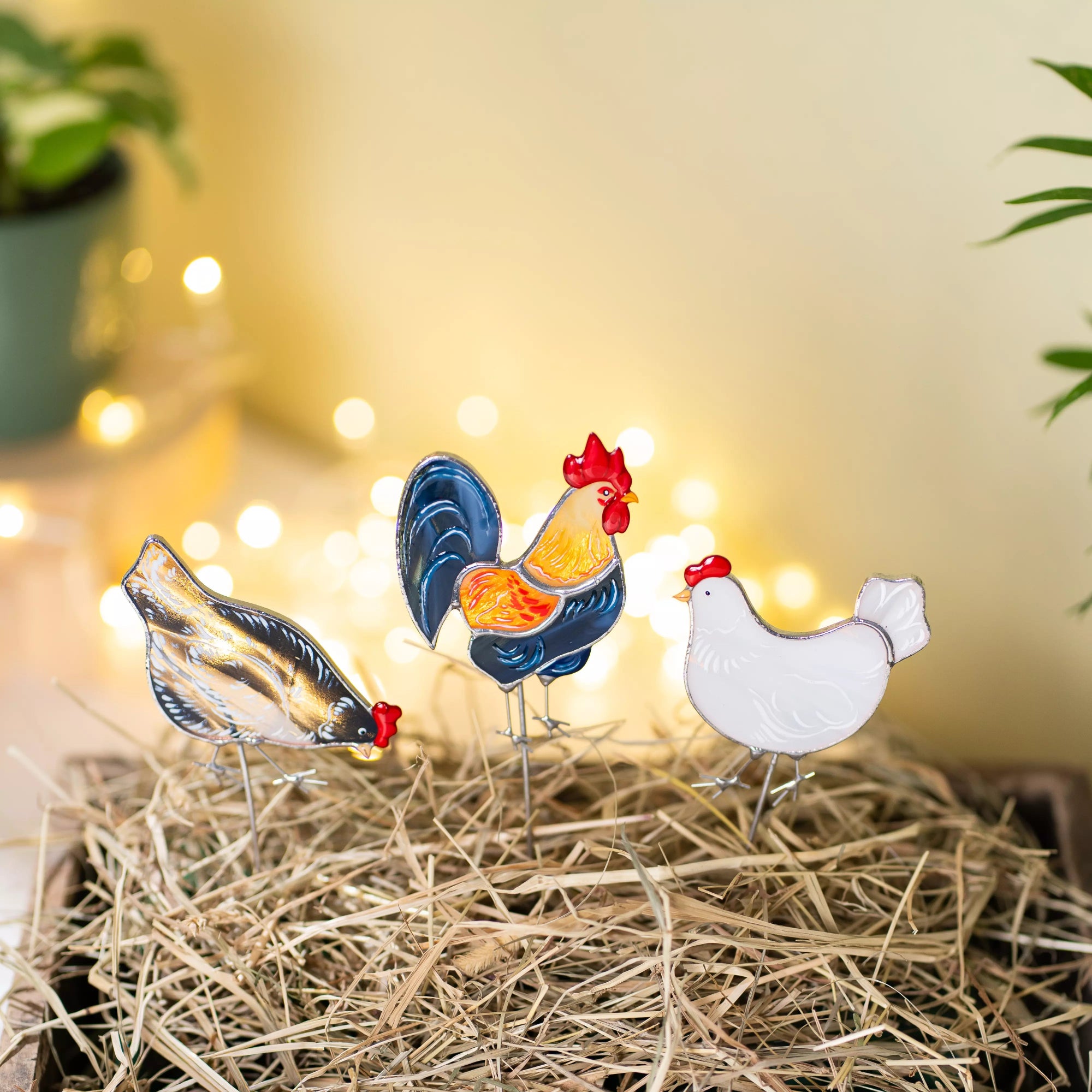 Decorative stained glass chicken figures on a bed of straw with a warm, blurred background.