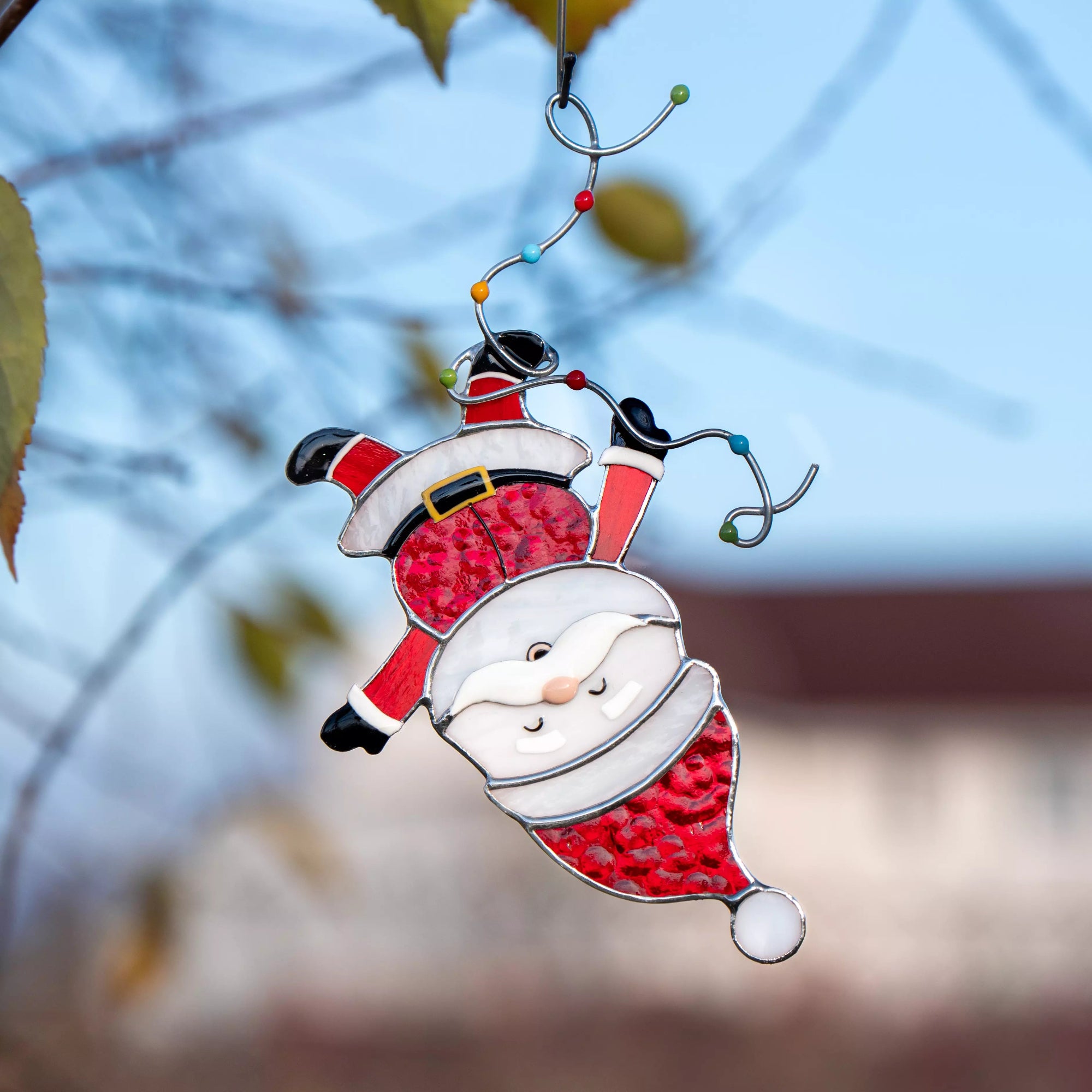 Stained glass suncacther of a Santa Claus figure hanging against a blurred natural background.