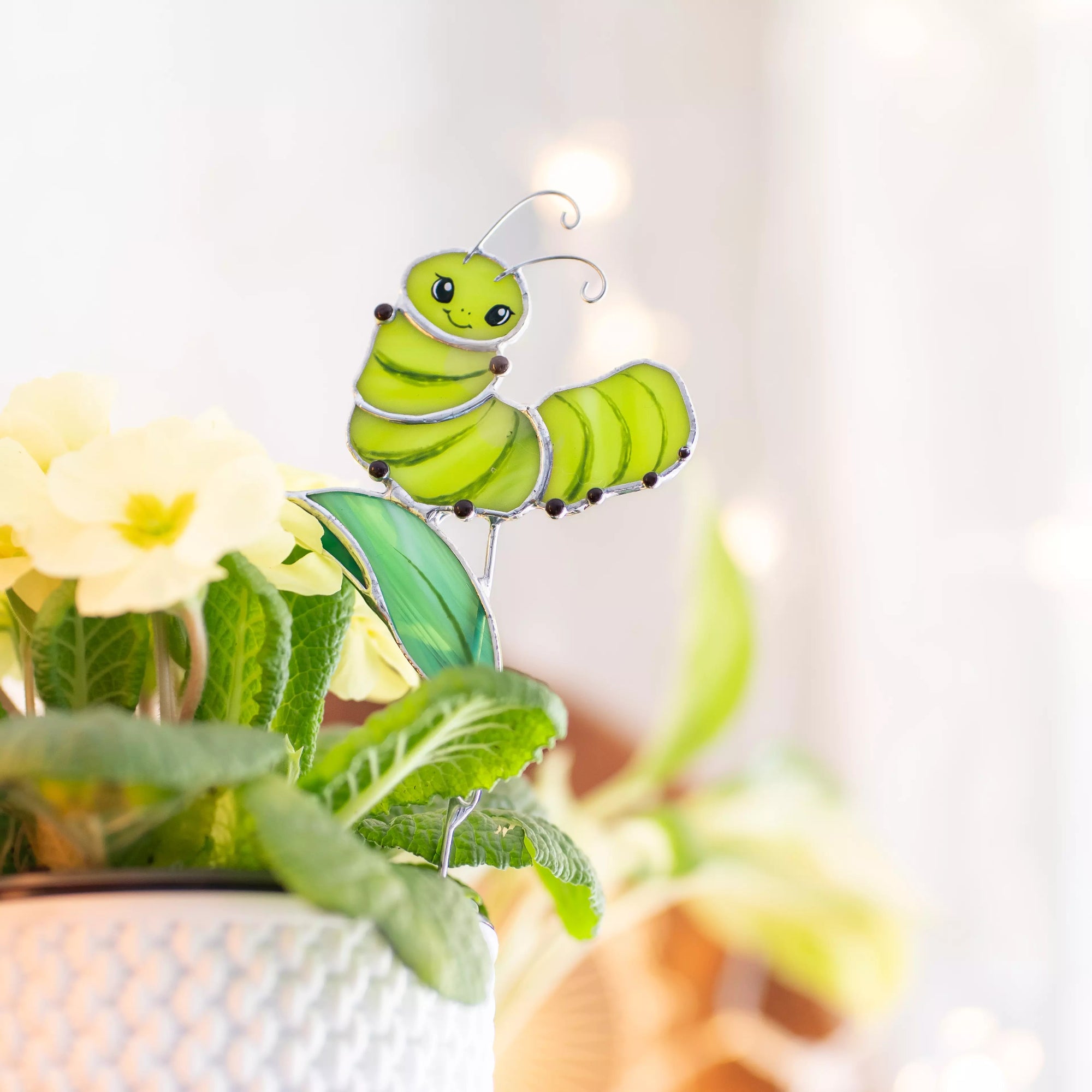 Stained glass green caterpillar plant stake ornament on a plant with a blurred background