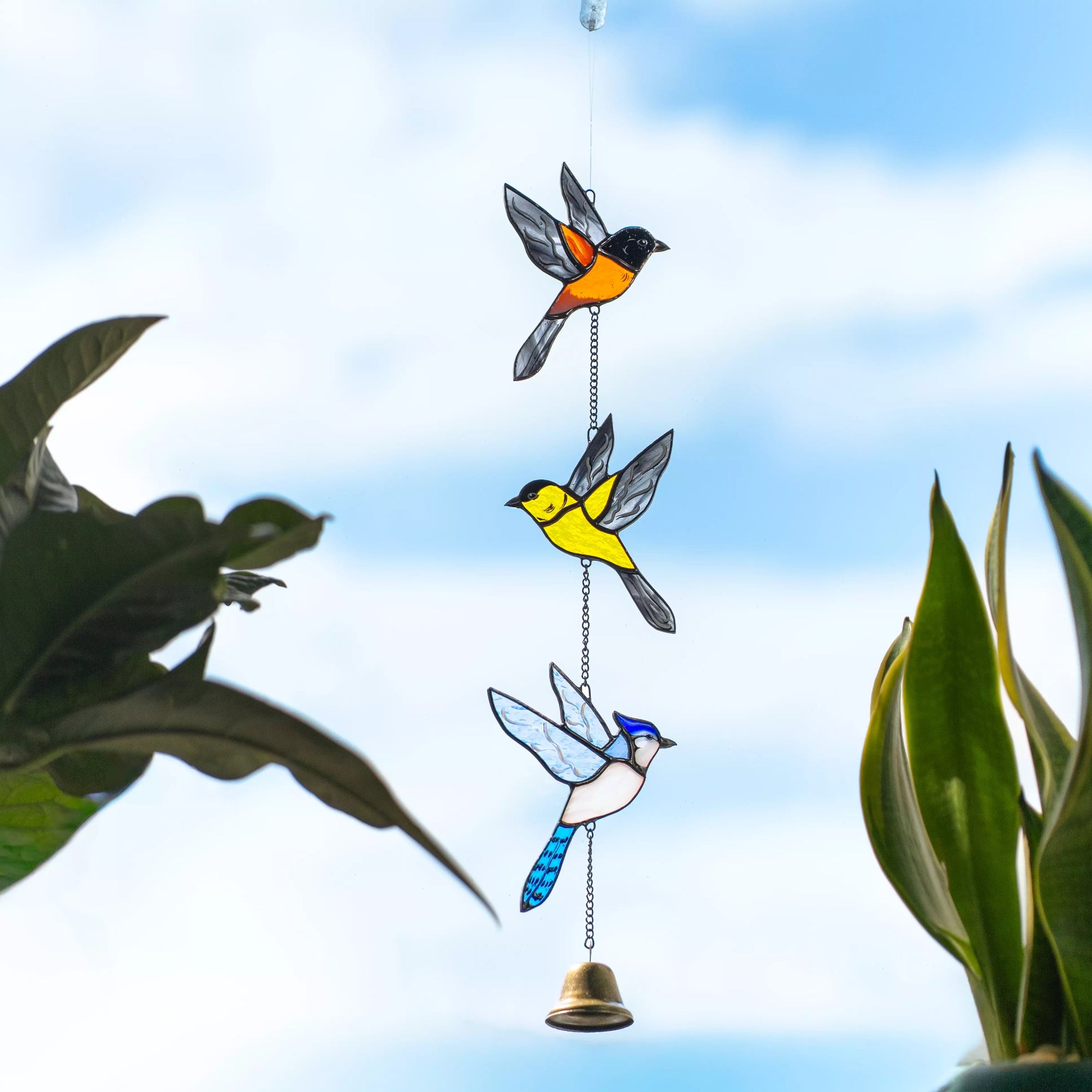 Stained glass window hanging bird ornament with a bell against a blue sky background