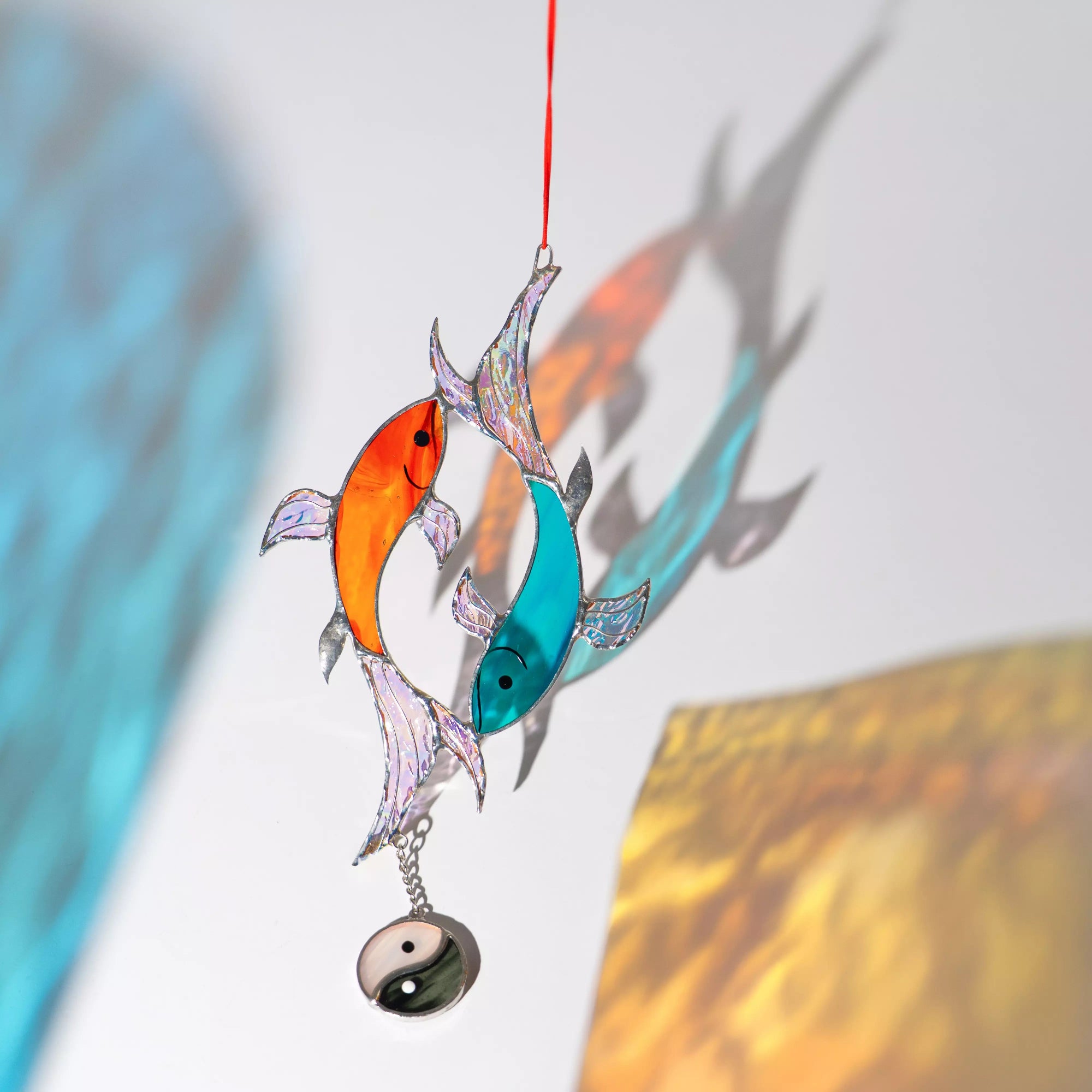 Stained glass ornament with two glass fish and a yin yang symbol casting a colorful shadow on a white surface