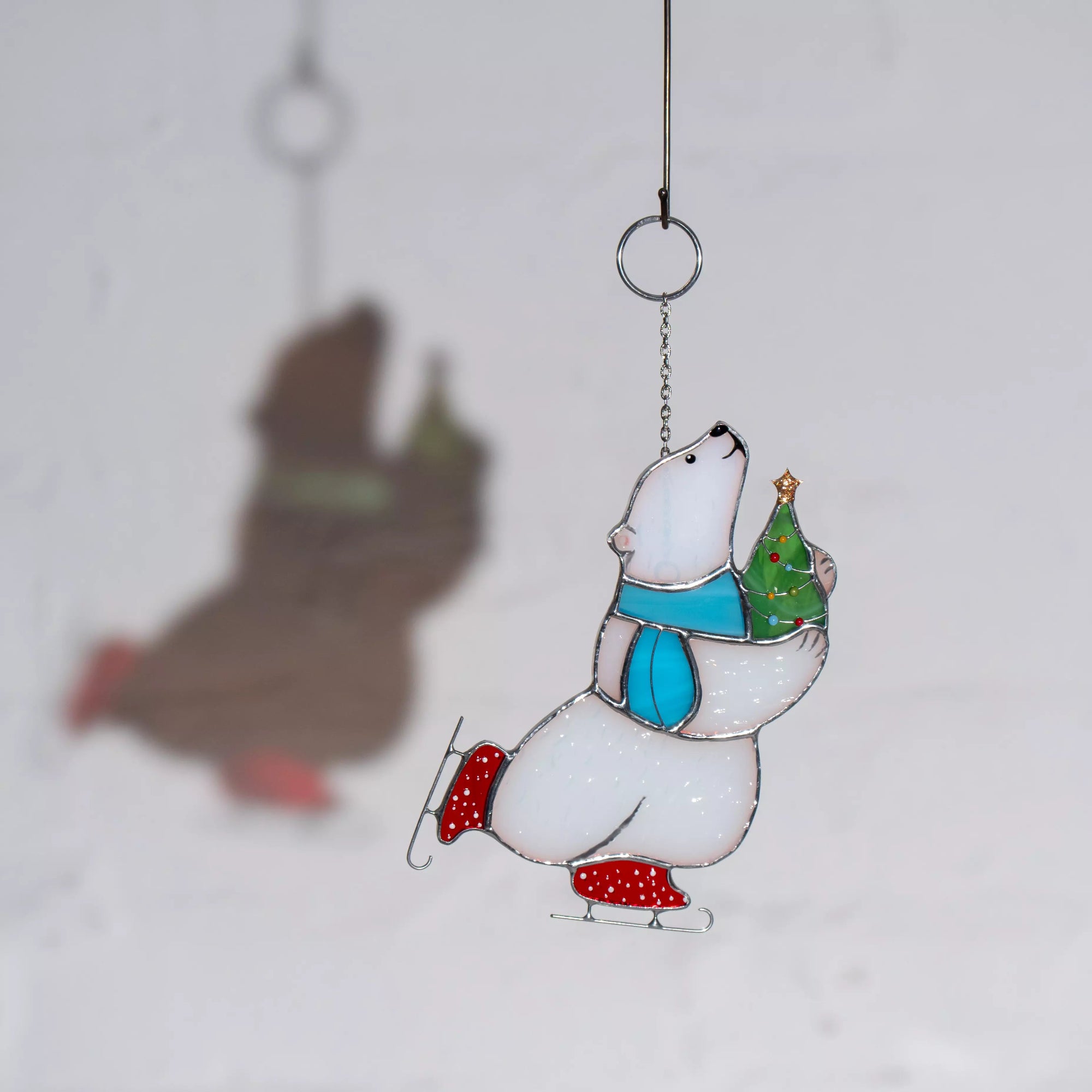 Stained glass window hanging polar bear ornament with a Christmas tree, casting a soft shadow on a white background