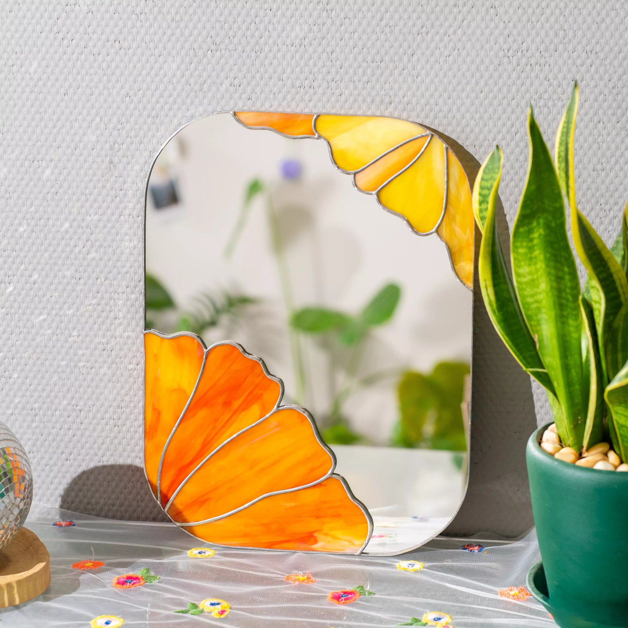 Stained glass mirror with butterfly design on a surface with a plant in the background