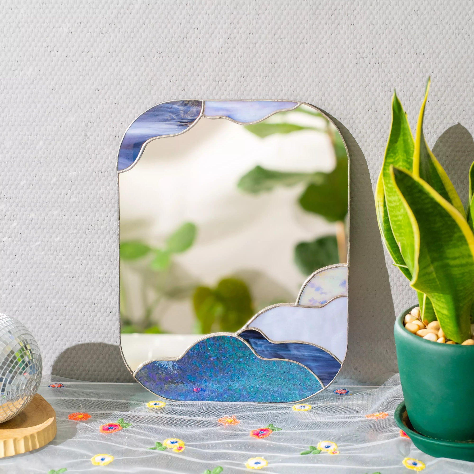 Stained glass mirror with cloud design on a table with a plant and colorful objects.