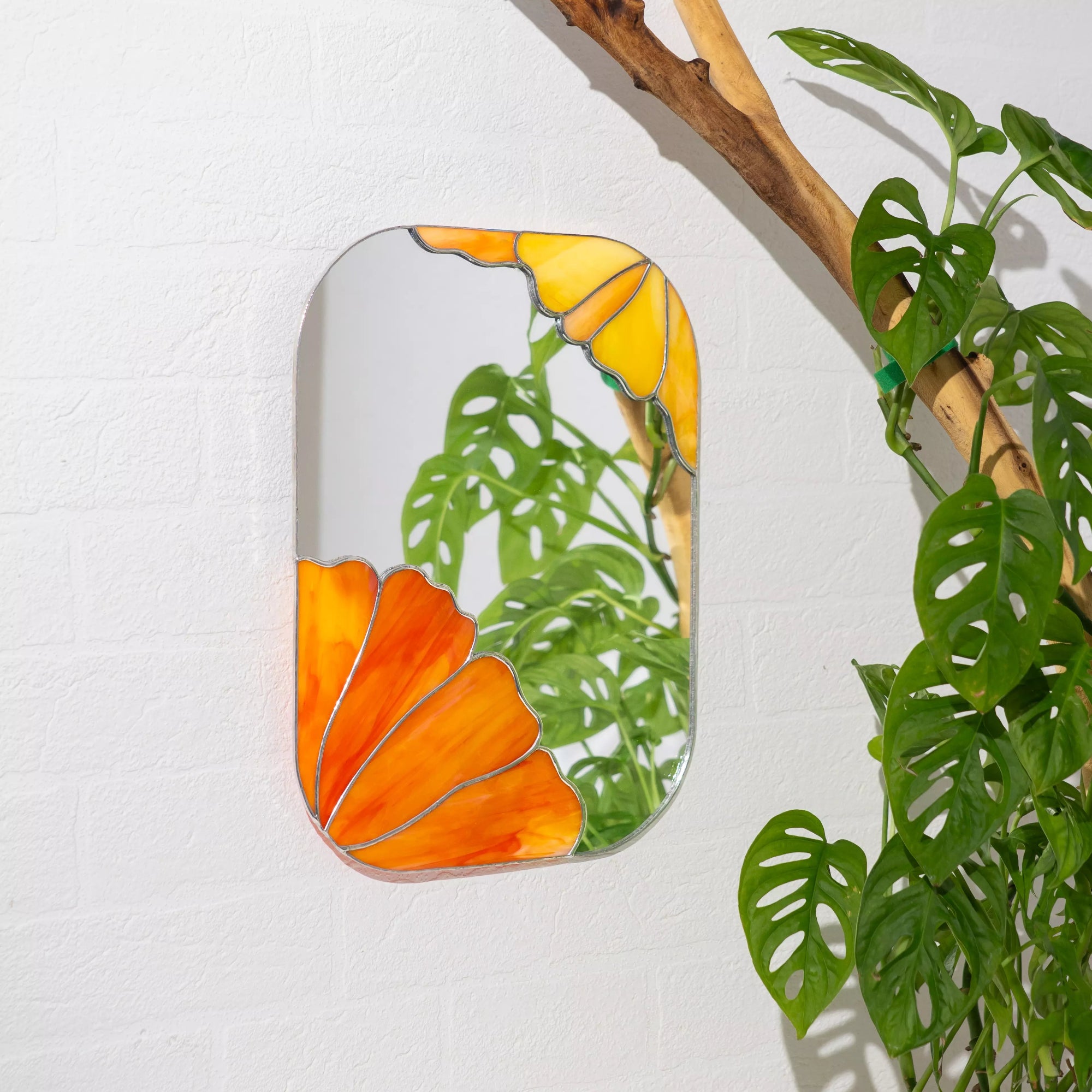 Stained glass mirror with orange and yellow floral design on a white wall with a plant.
