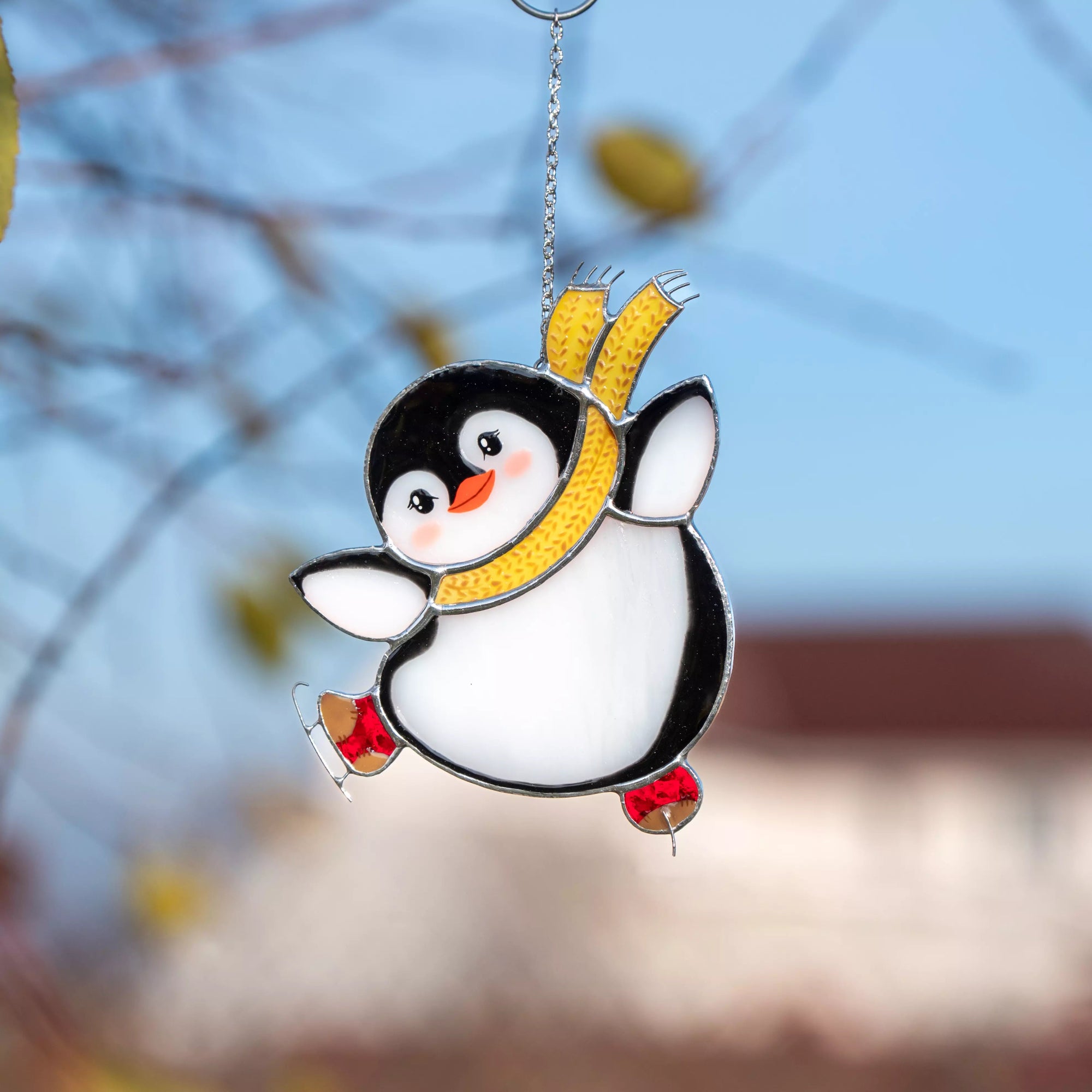 Stained glass penguin ornament with a yellow scarf against a blurred natural background
