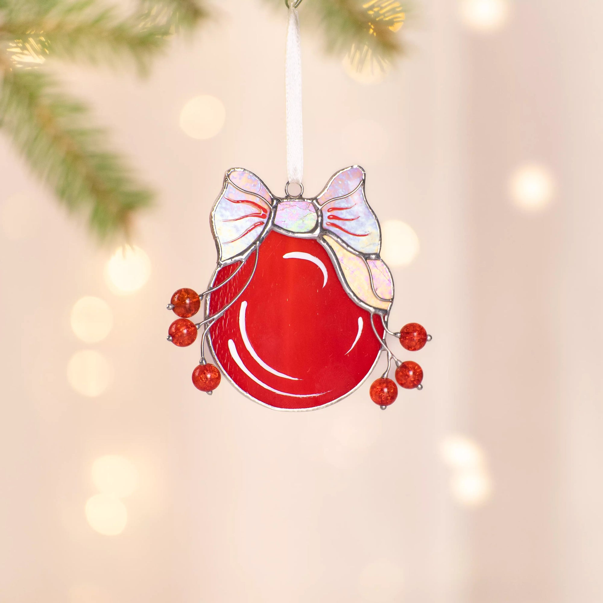 Stained glass red ball ornament with iridescent hanging against a blurred Christmas tree background.