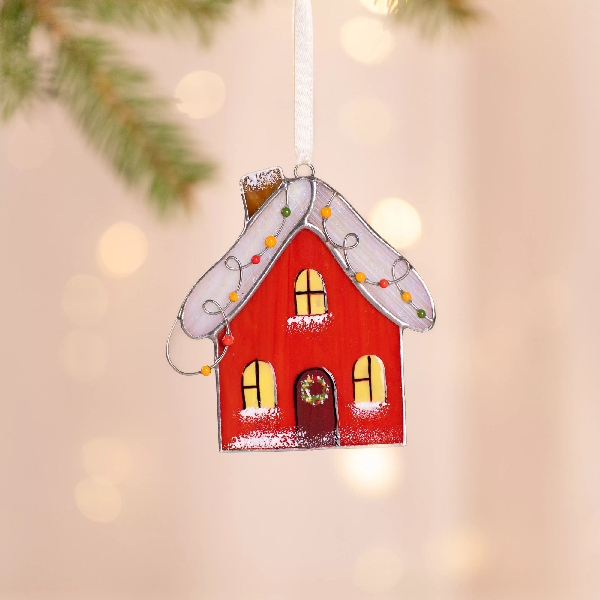 Decorative red gingerbread house stained glass ornament with a wreath on a blurred background