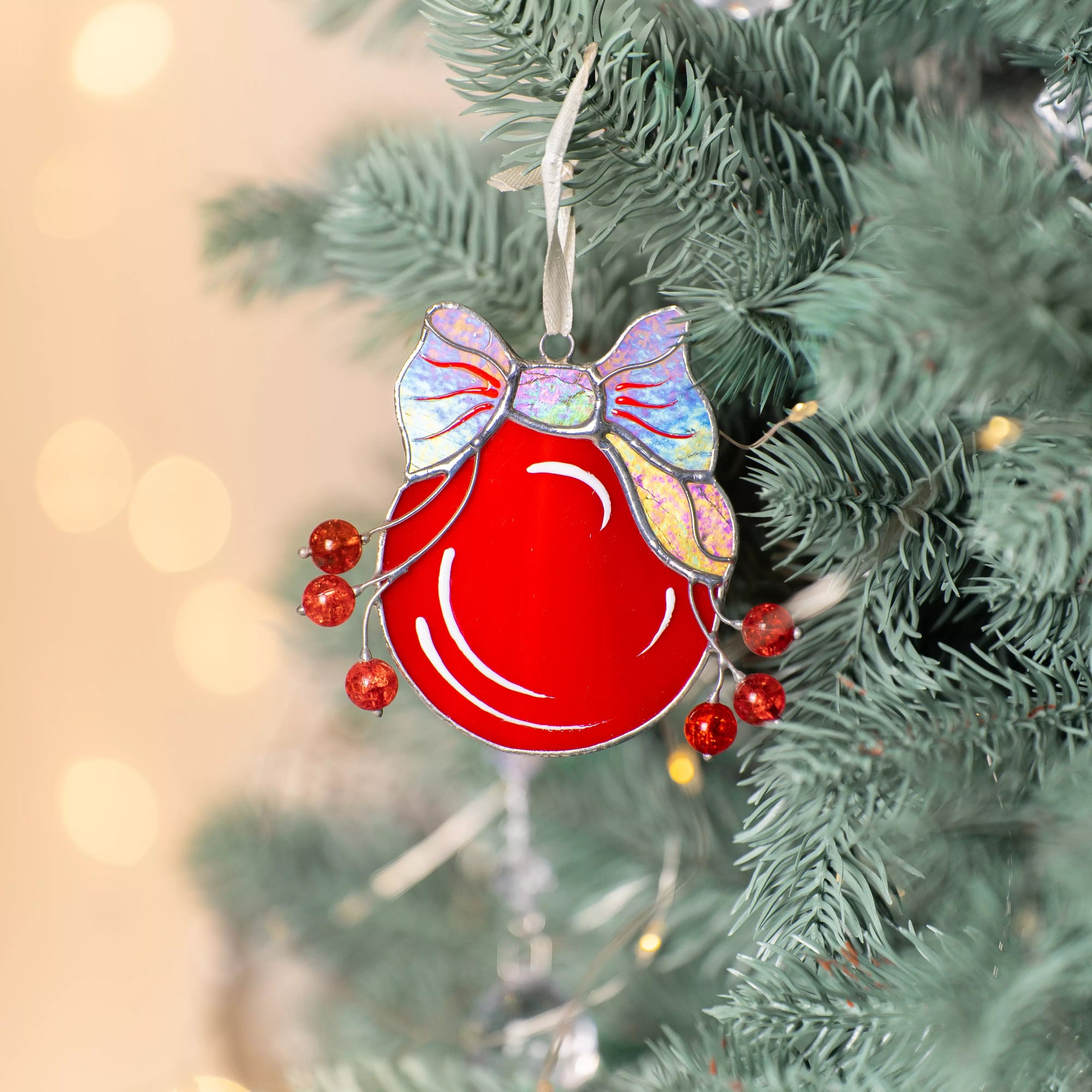 Stained glass red ornament with a bow and beads on a Christmas tree.