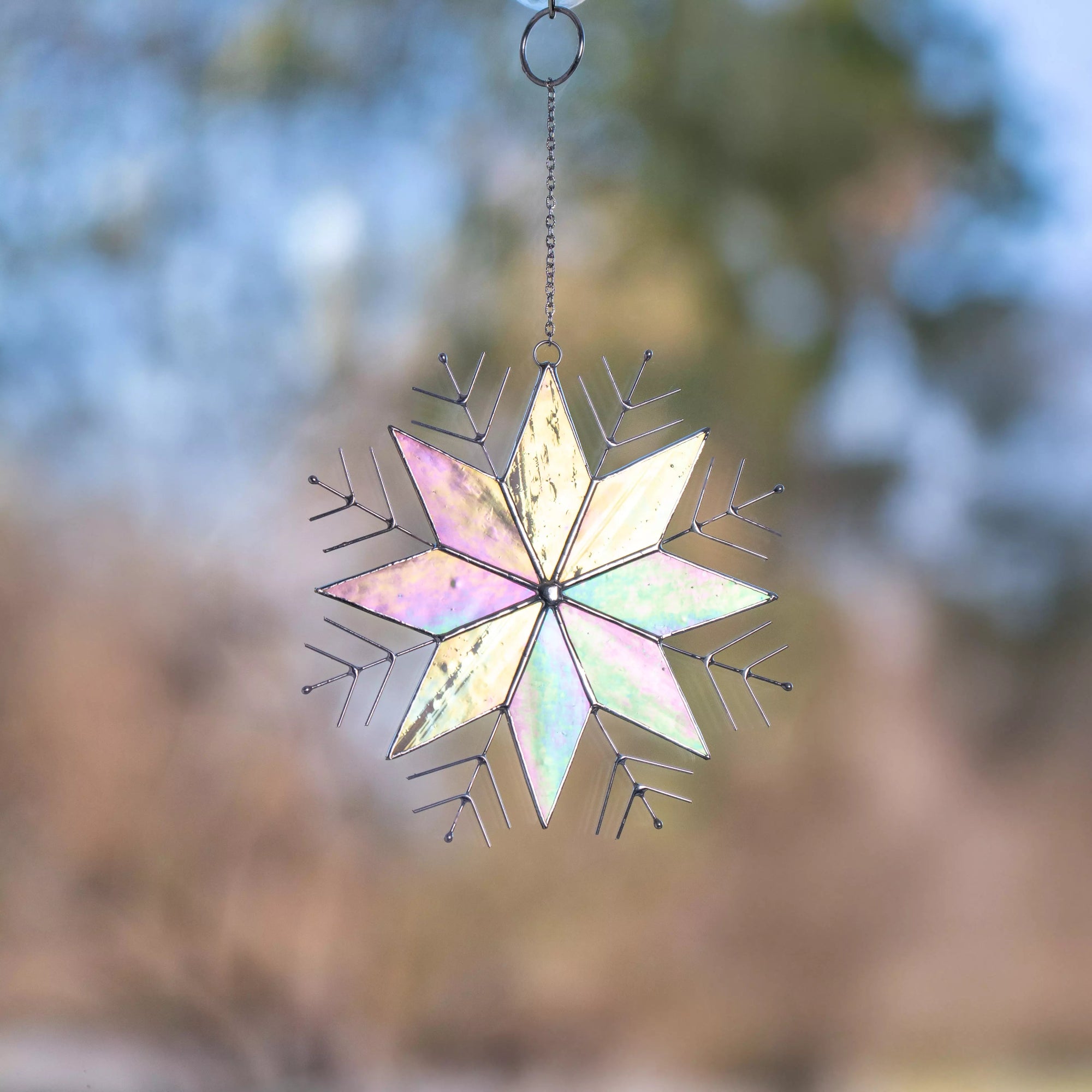 Decorative snowflake suncatcher with iridescent colors hanging on a window against a blurred natural background