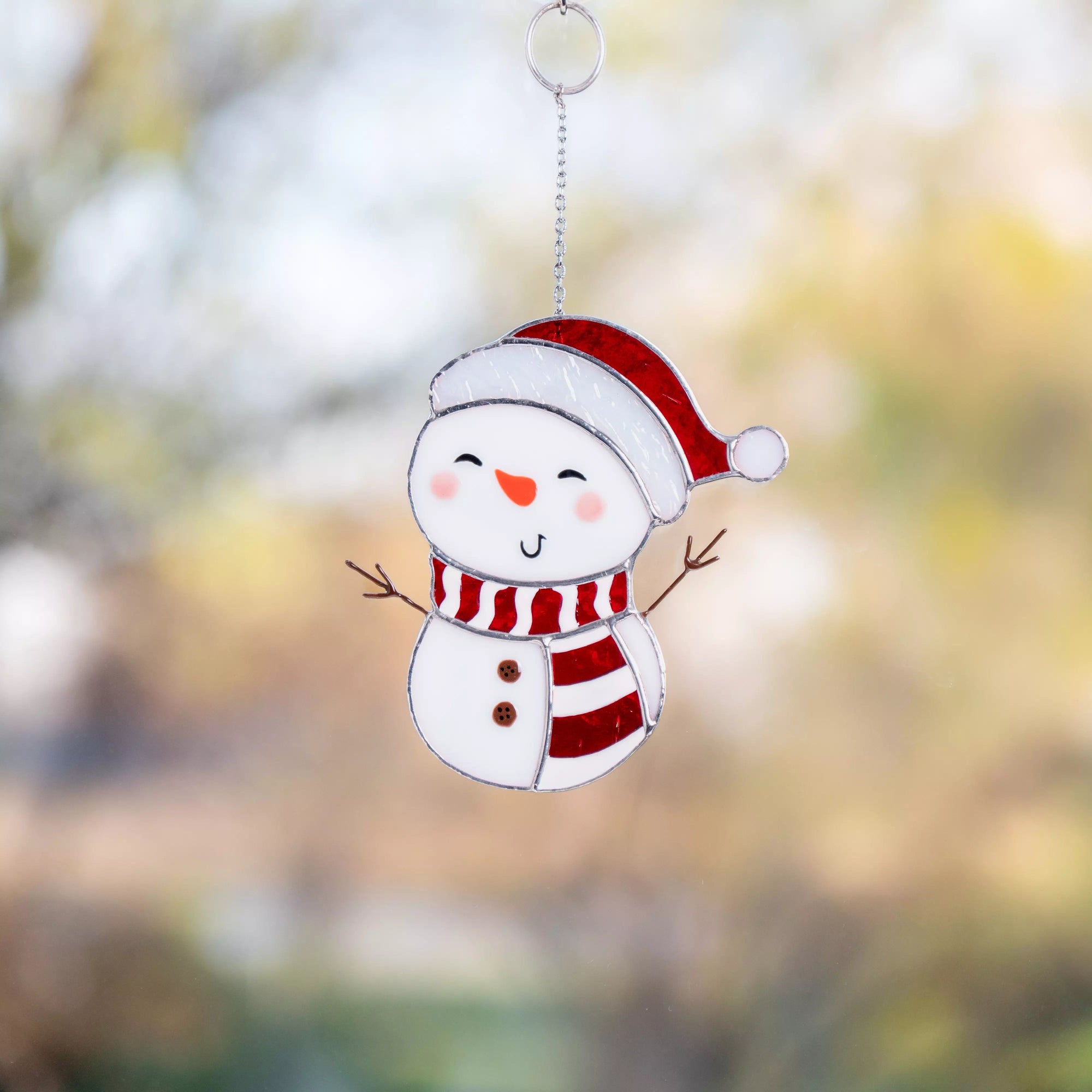 Snowman stained glass suncatcher with a Santa hat against a blurred natural background