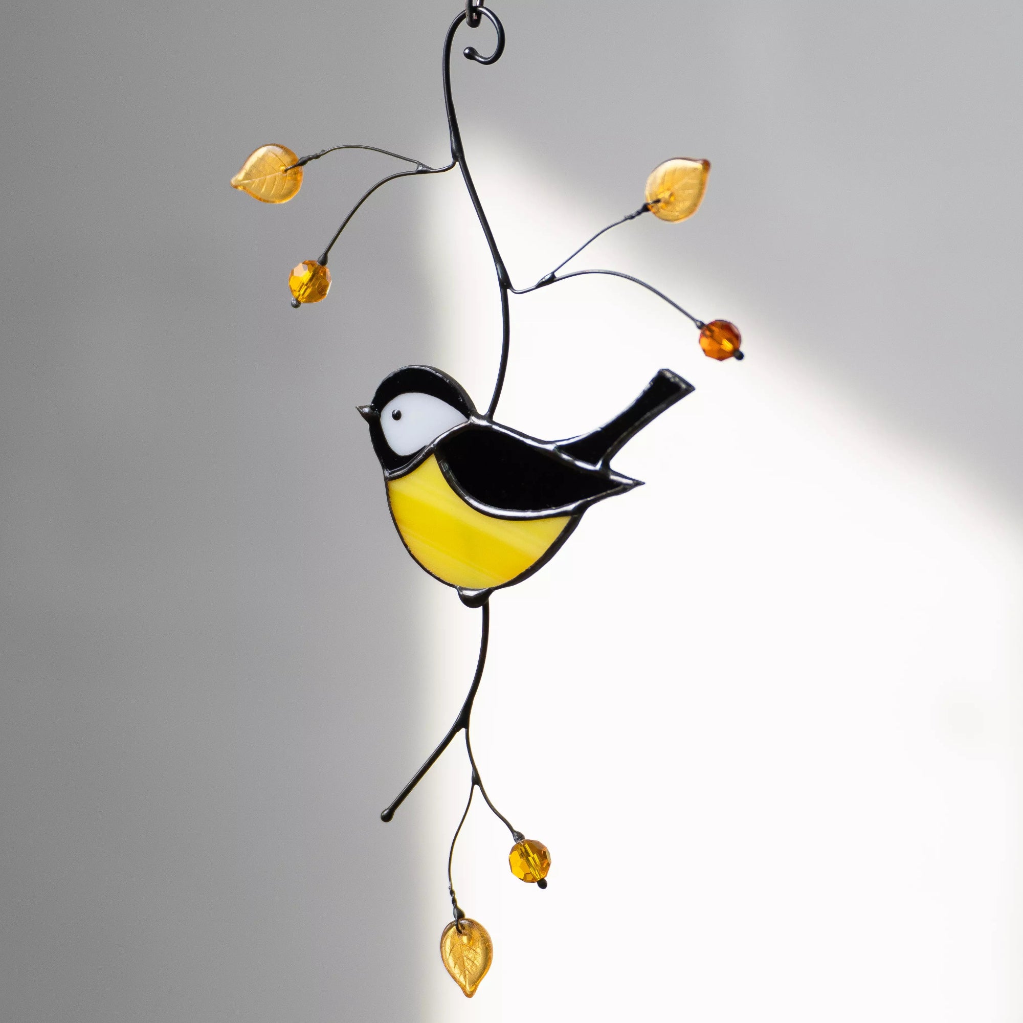 Decorative stained glass chickadee bird on a branch with yellow leaves against a shadow