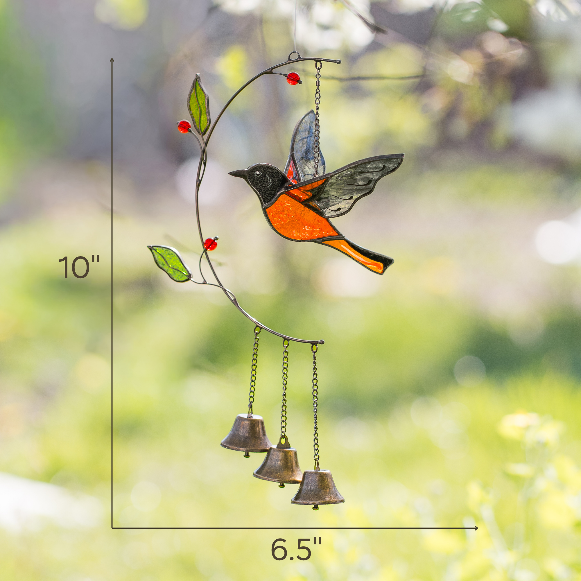 Stained glass baltimore oriole with bells on a branch against a blurred natural background