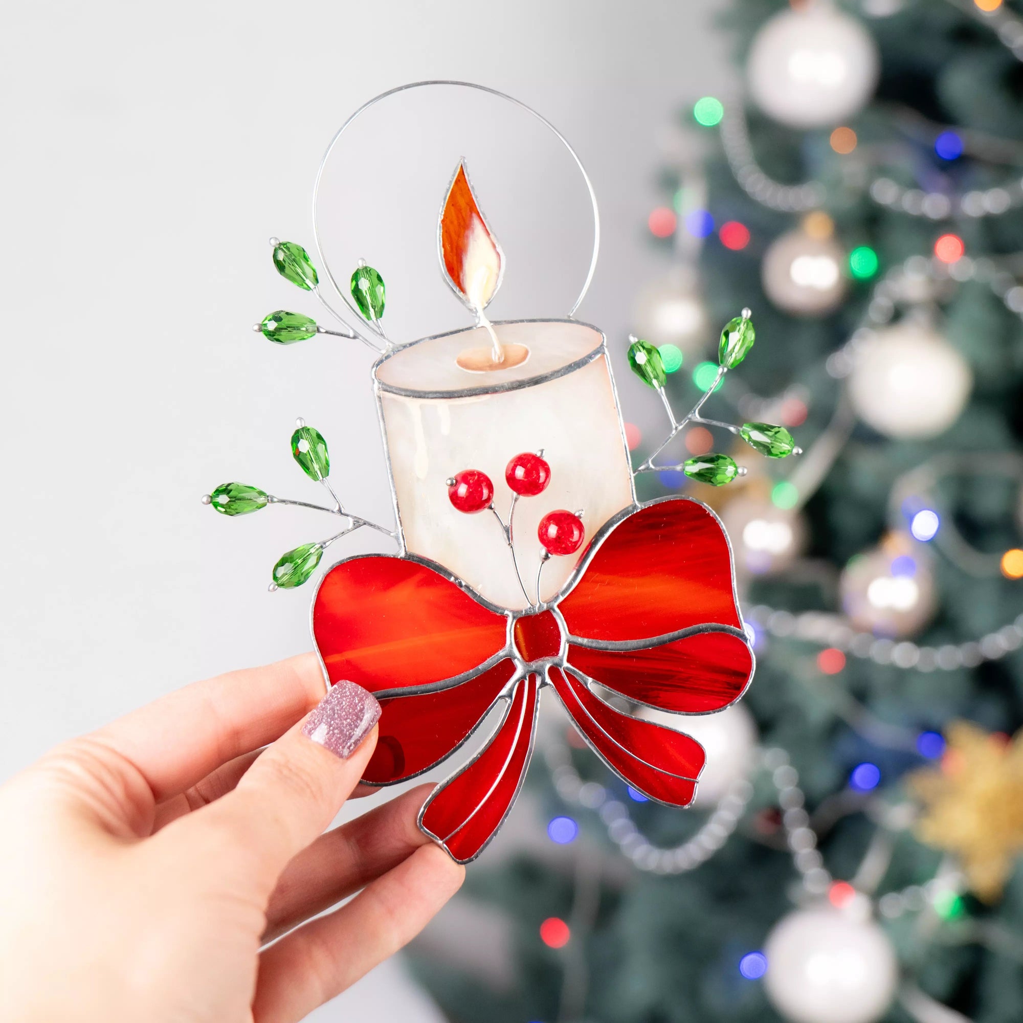 Stained glass ornament candle with red bow held in front of a Christmas tree.