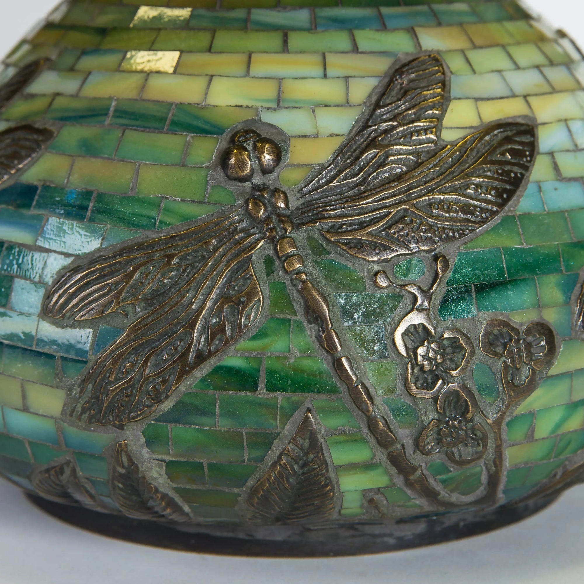 Detail of bronze-tone dragonflies and floral design embedded in the green tiled lamp base
