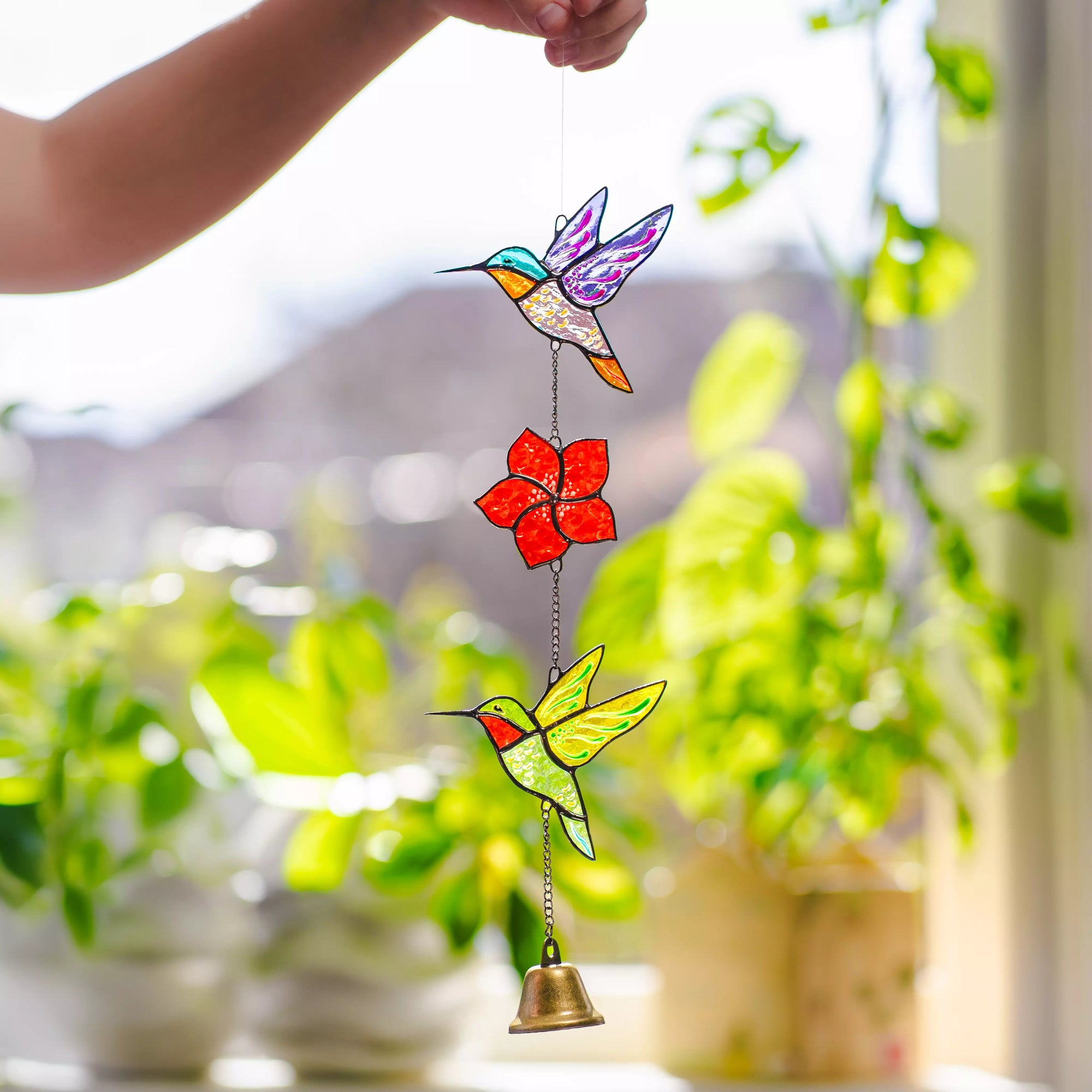 Stained glass hummingbird and flower hanging ornament with a blurred garden background.
