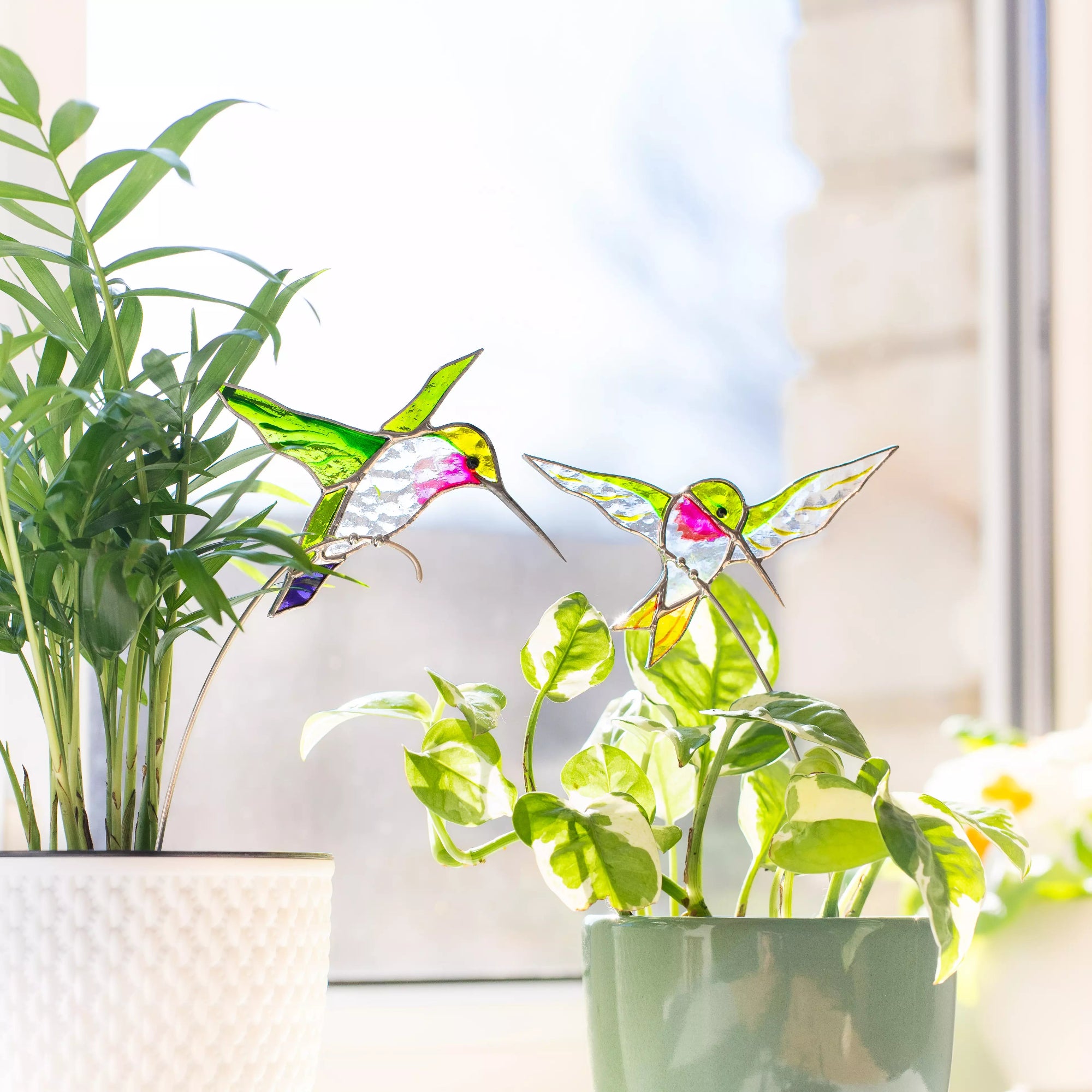 Stained glass hummingbird plant stakes with a blurred indoor background