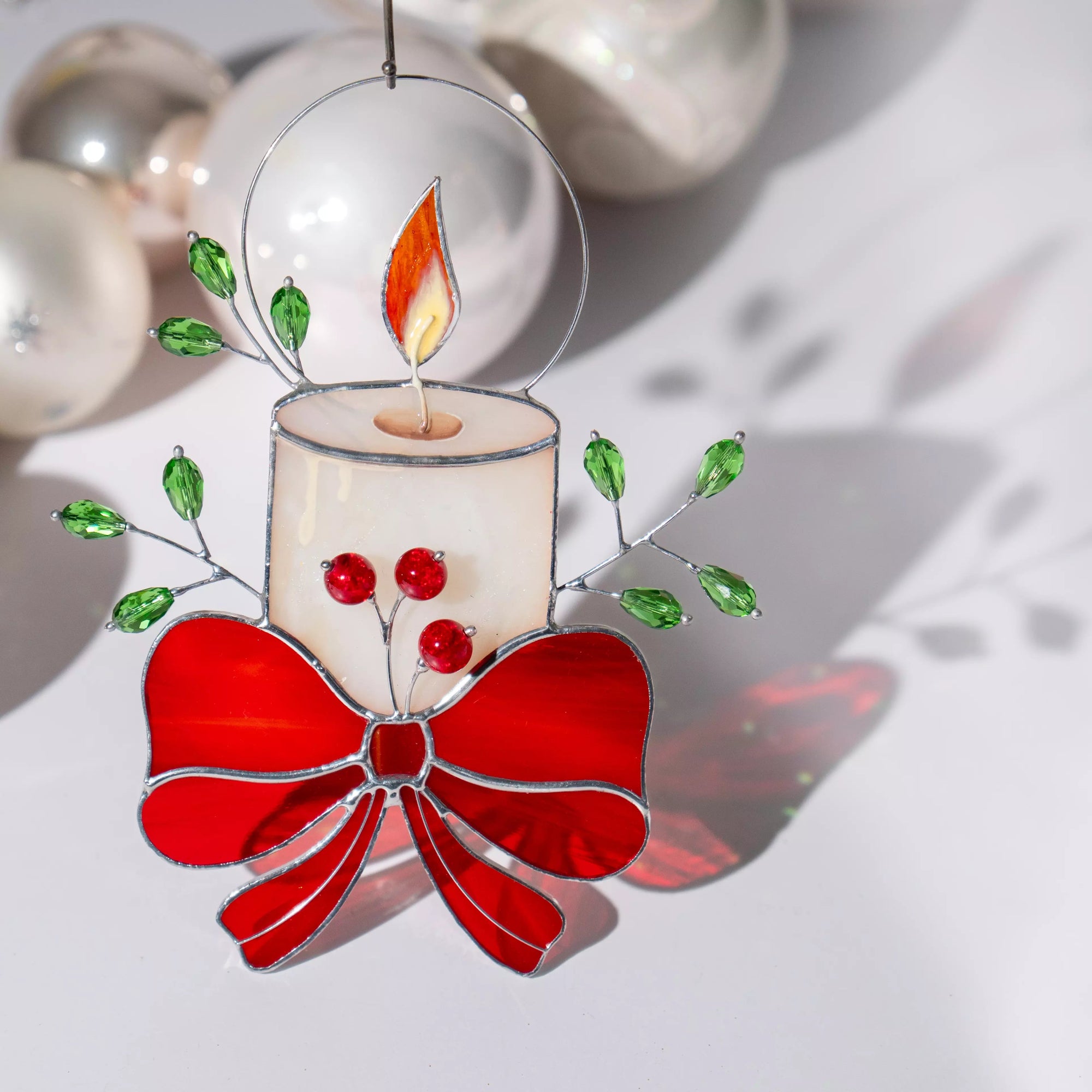 Decorative stained glass ornament featuring a candle with red bow, casting a soft shadow