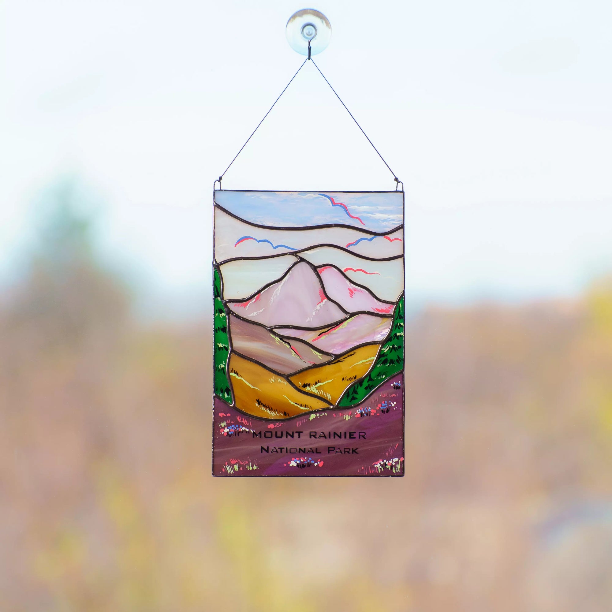 Stained glass panel of Mount Rainier with a blurred natural background