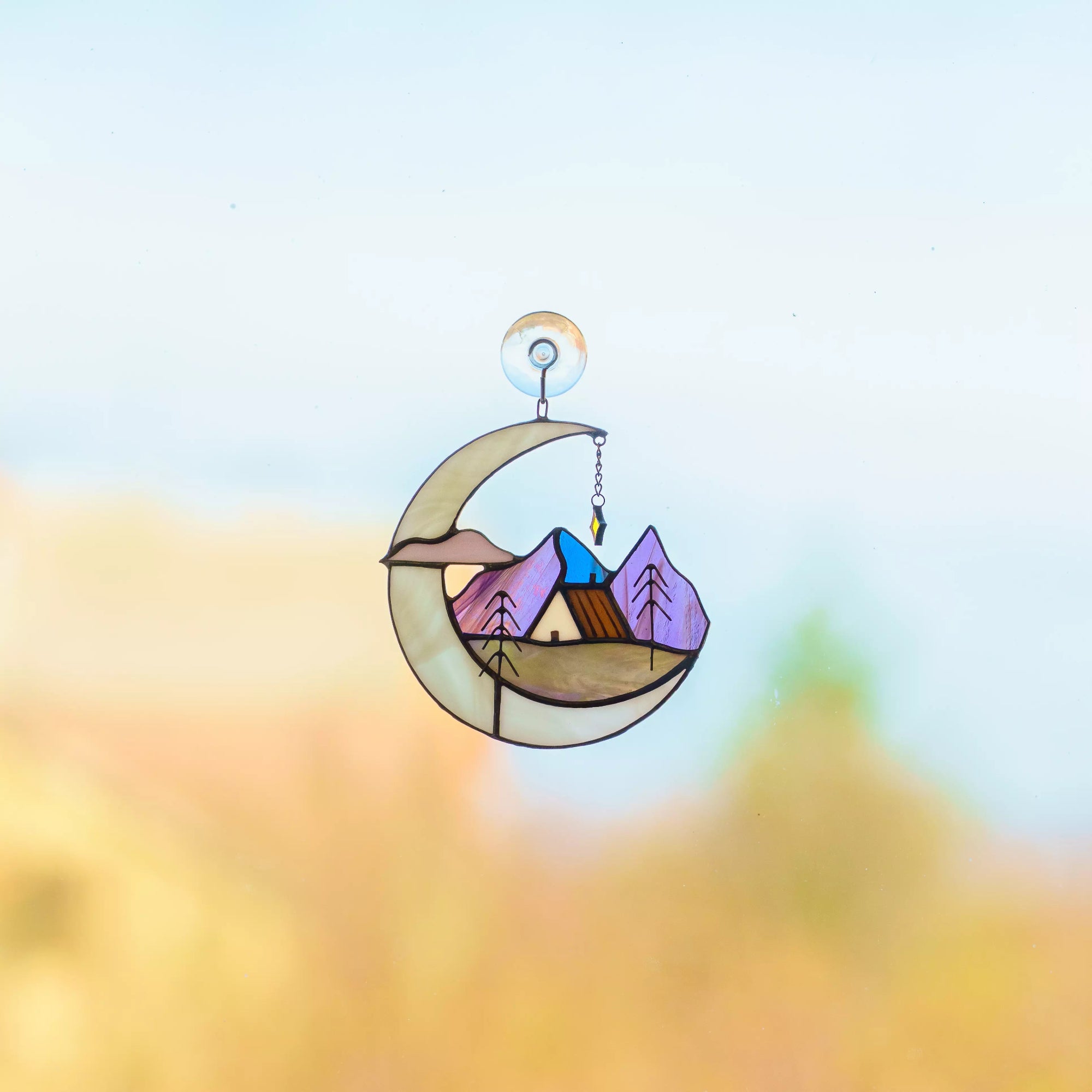 Stained glass suncatcher with a crescent moon, mountain landscape, and house.