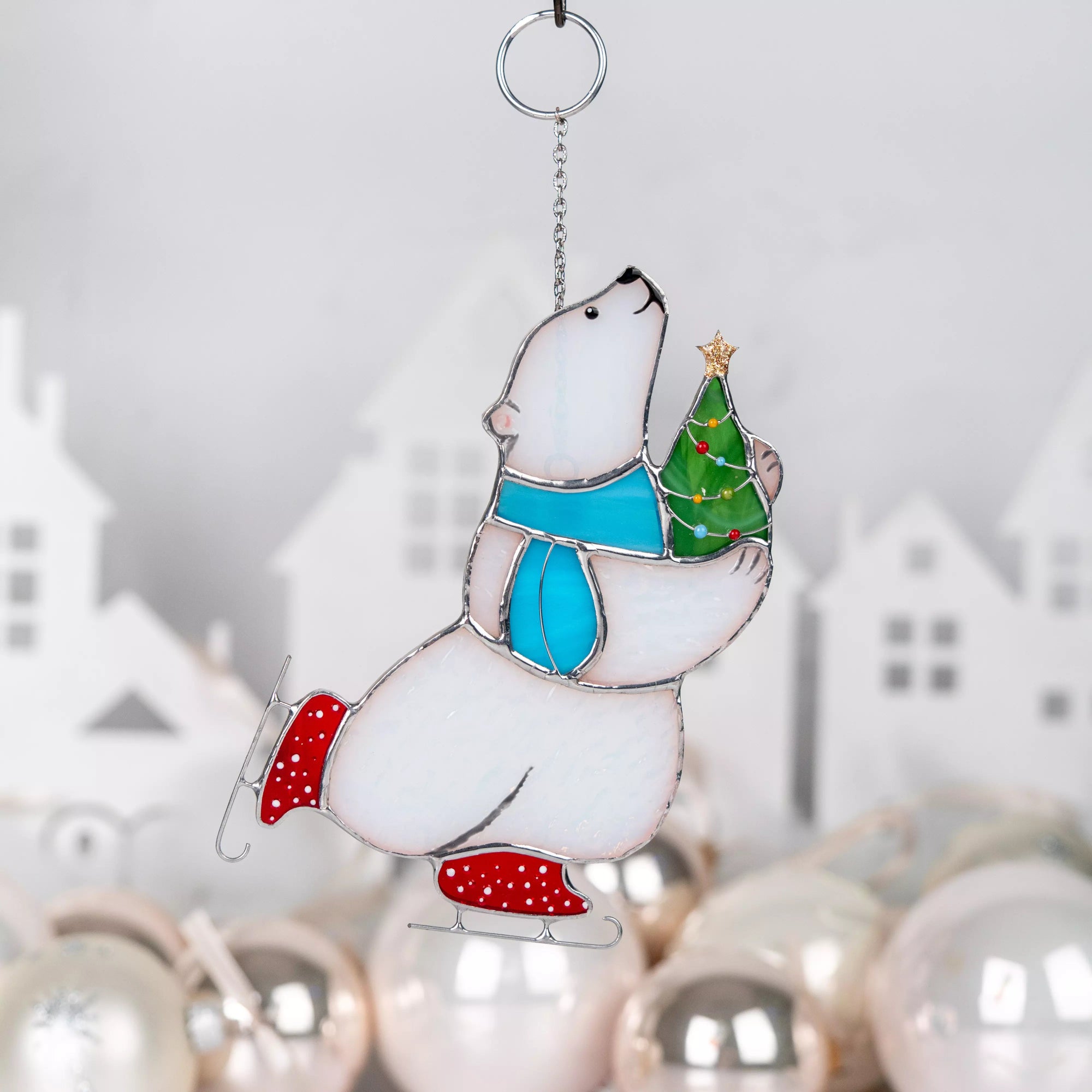 Stained glass polar bear on a skates with a Christmas tree, hanging against a blurred festive background.