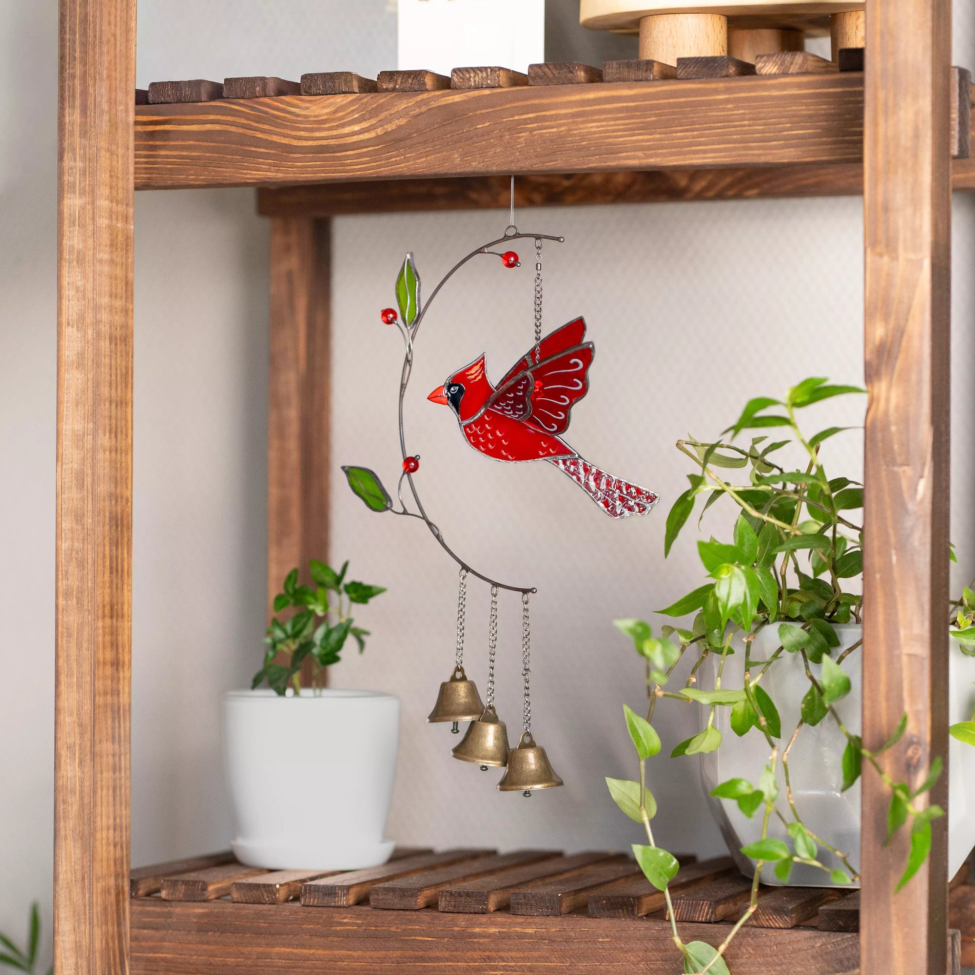 Stained glass wind chime with a red cardinal design on a wooden shelf.