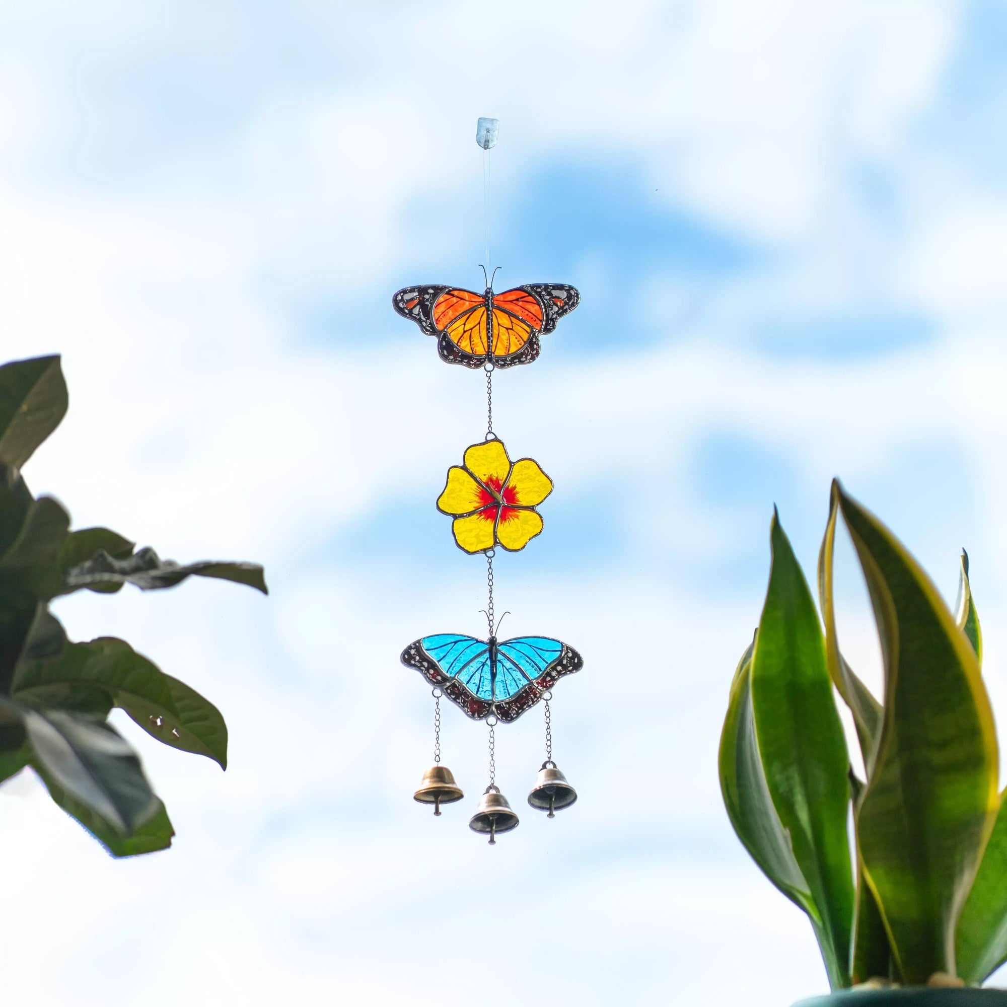 Stained glass wind chime with butterfly and flower design against a blue sky.