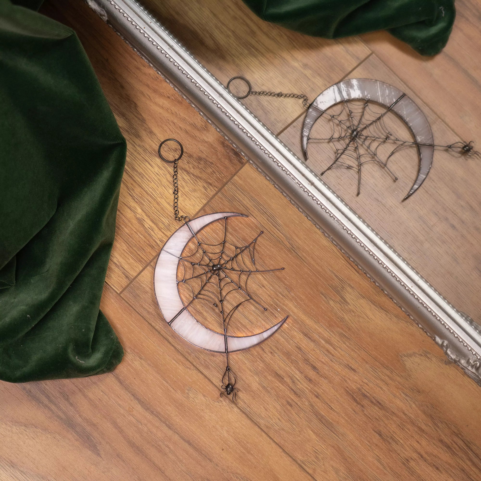 Decorative stained glass window hanging with moon and spider web design on a wooden surface.