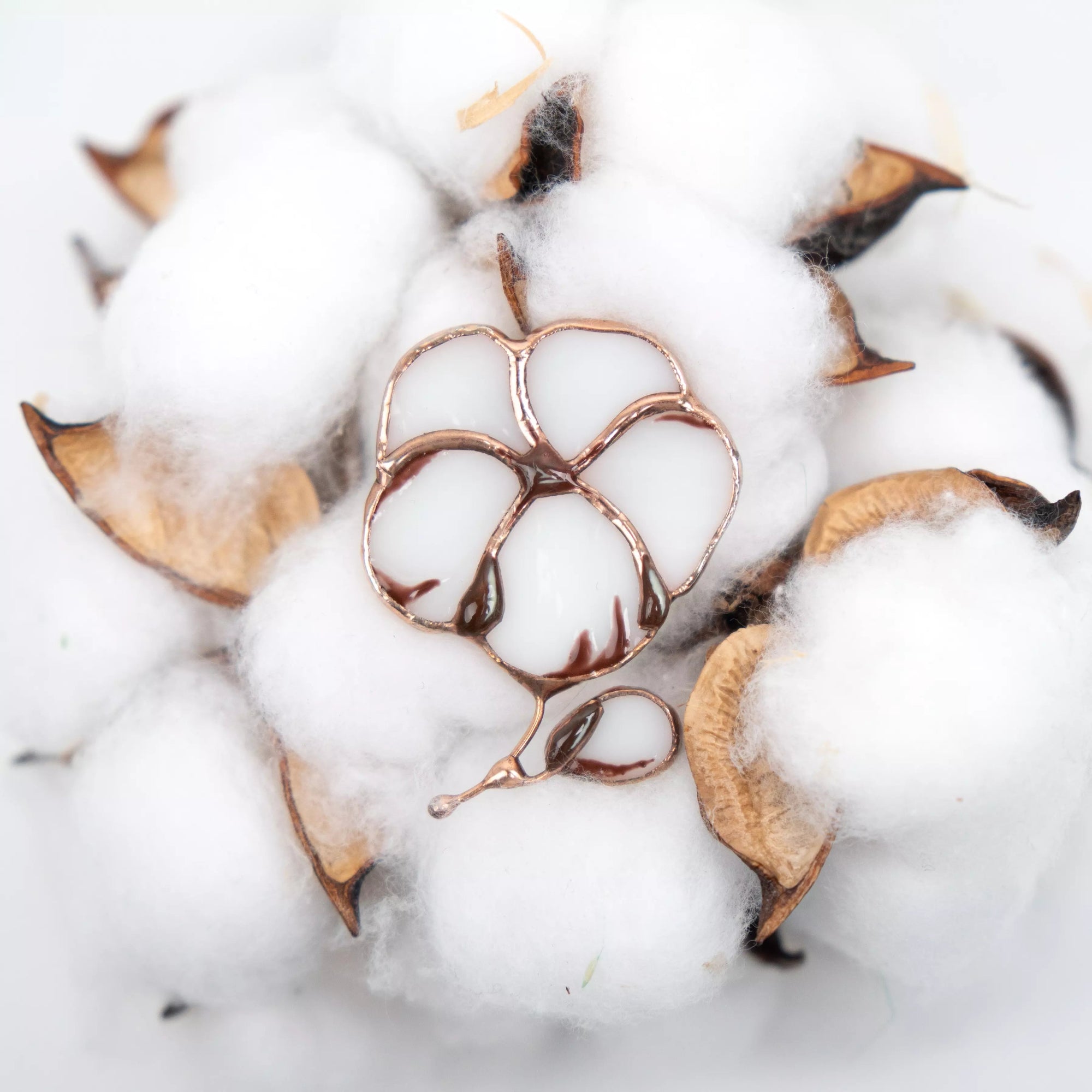 Stained glass cotton brooch placed on fluffy white cotton bolls with brown husks for soft natural styling.