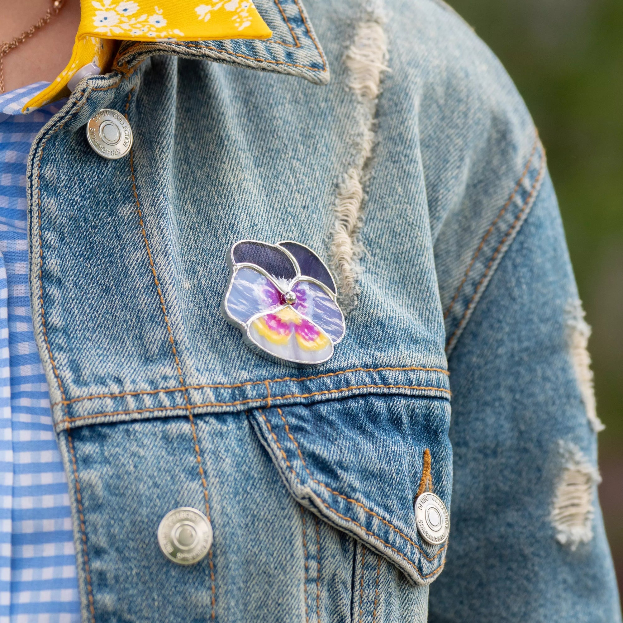 Denim jacket with a colorful pansy-shaped pin on a blurred background