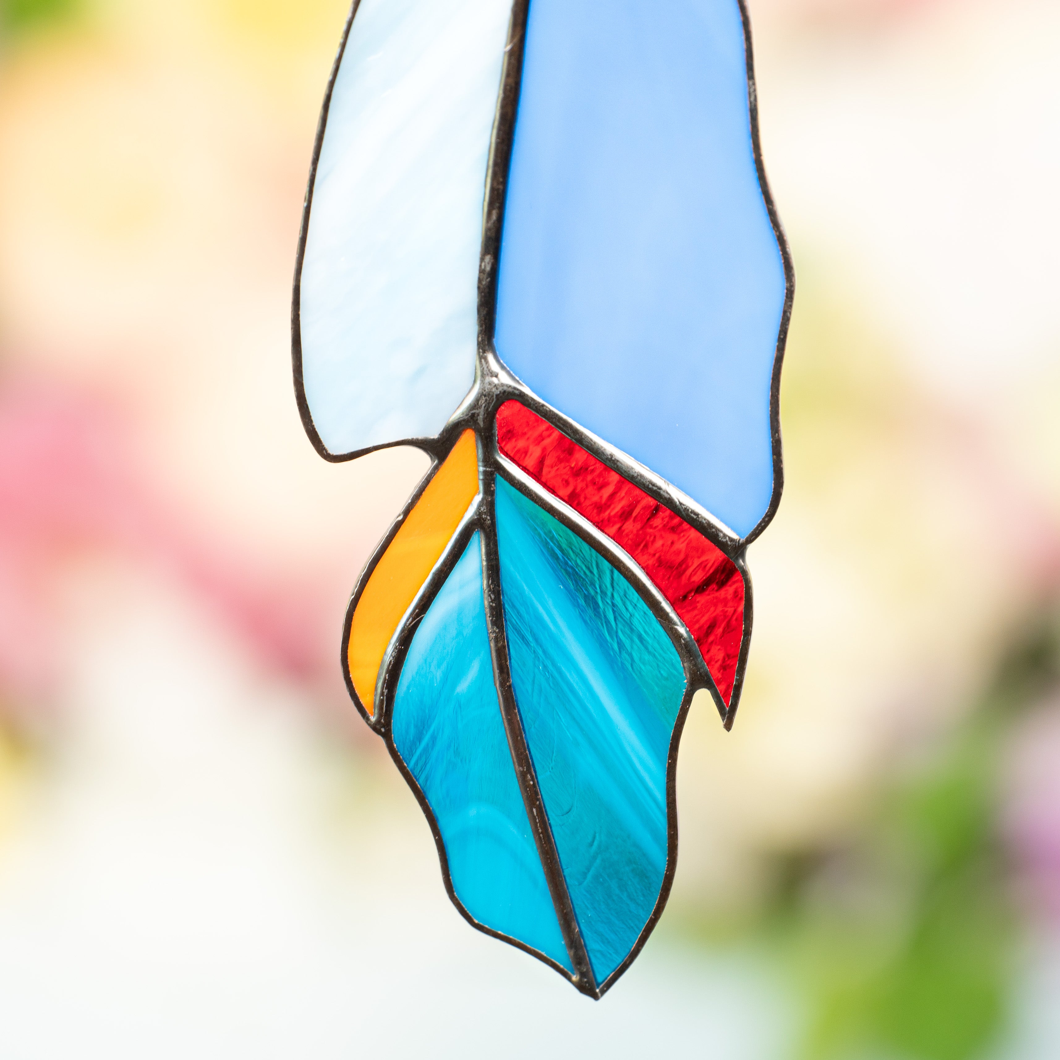 Close-up of the feather’s tip showing textured stained glass in bright red, orange, and teal.