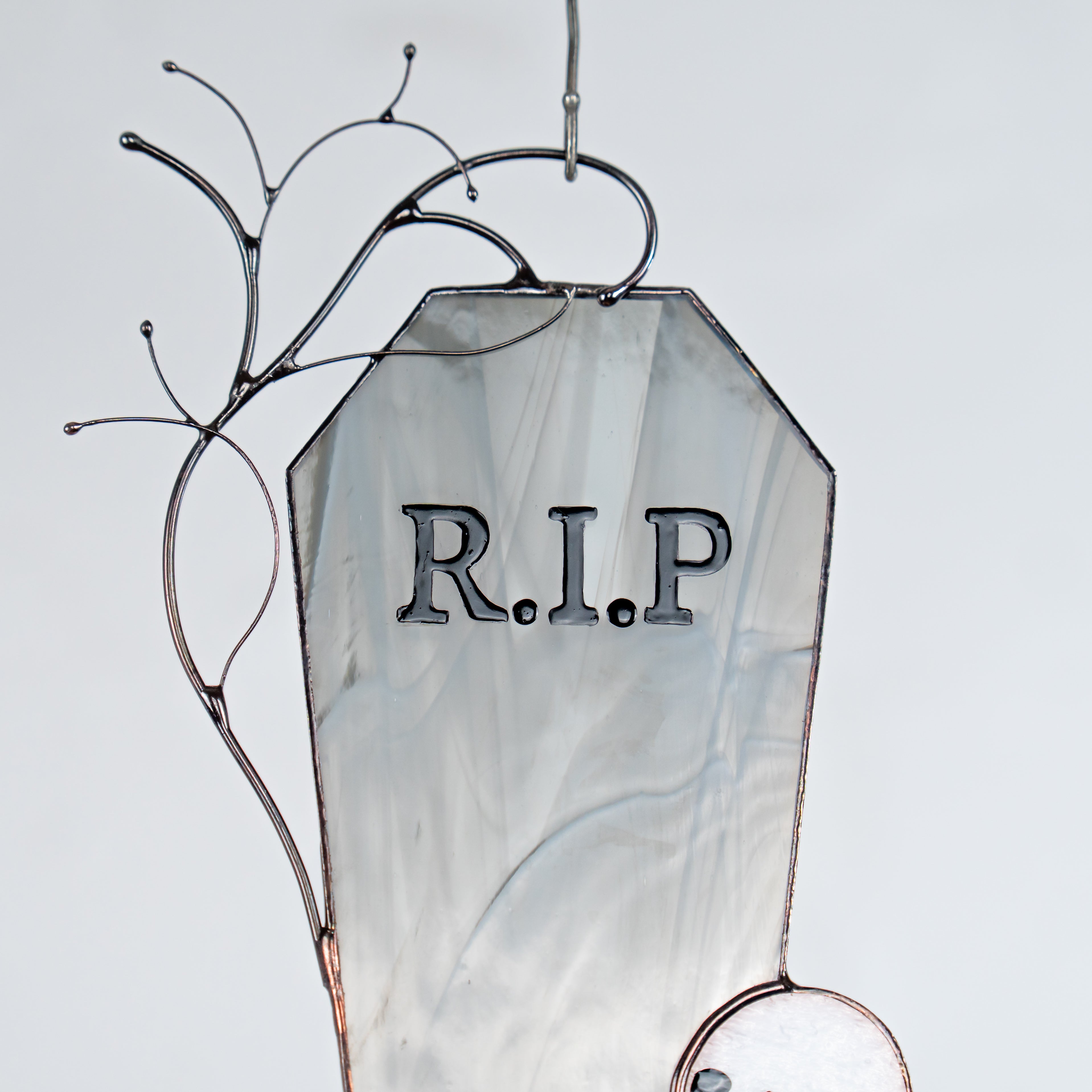 Close-up of top part of tombstone with painted “R.I.P” letters in stained glass, with background in cool misty tones.